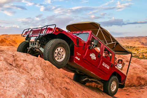 Red Hummer climbing a red rock hillside; passengers inside.