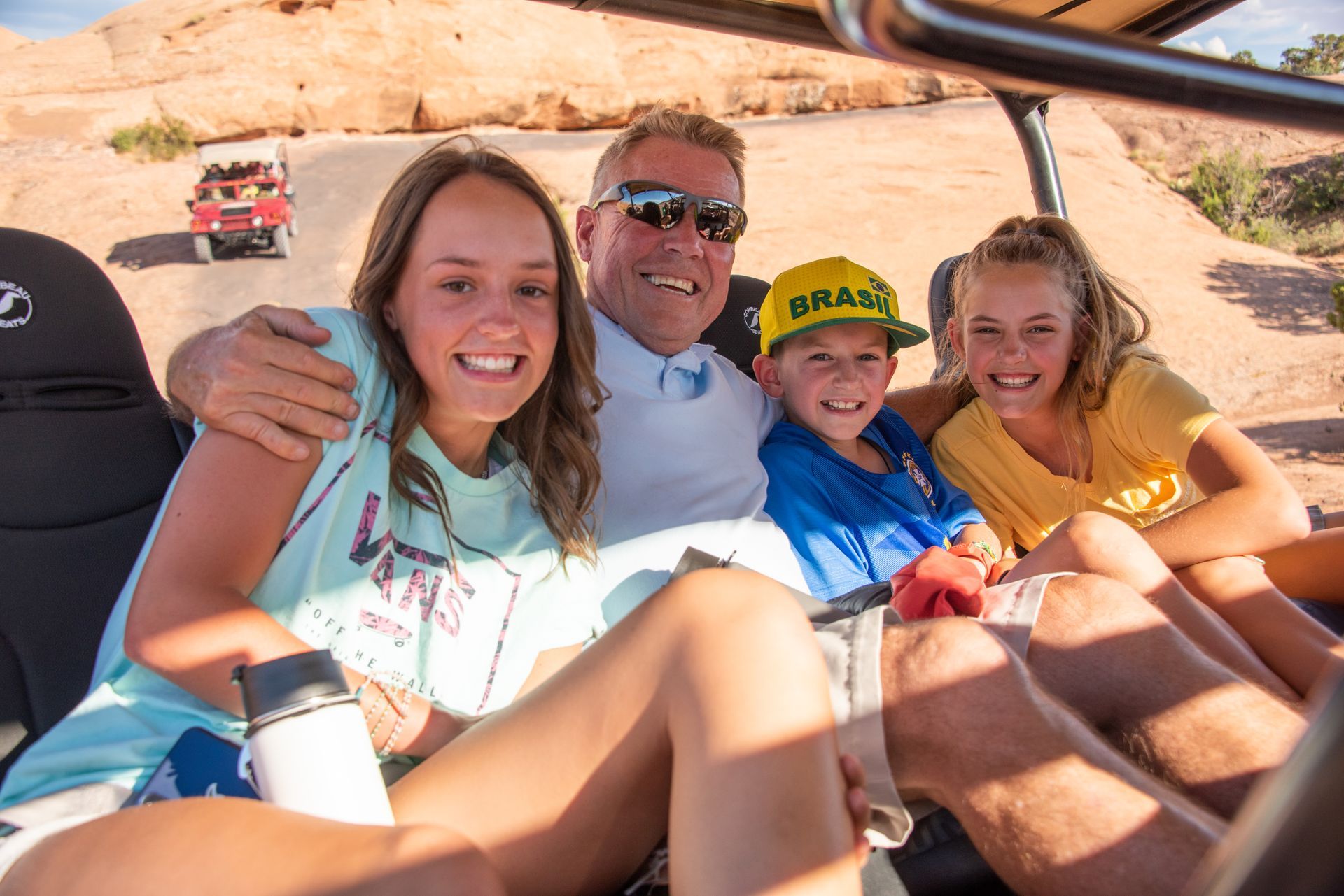 Family smiling on a Hummer Safari on a sunny day. Red rocks in the background.