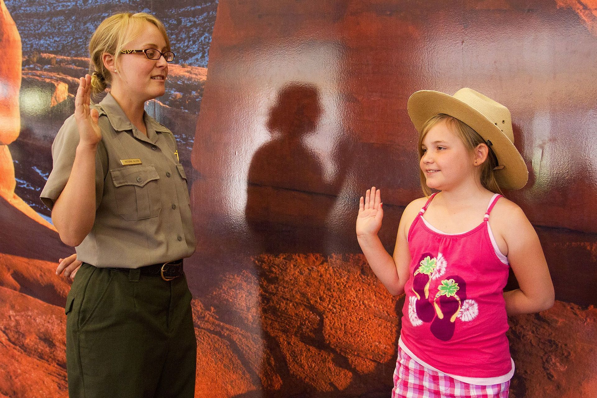Park ranger and girl taking oath, both with right hands raised, in front of a textured background.