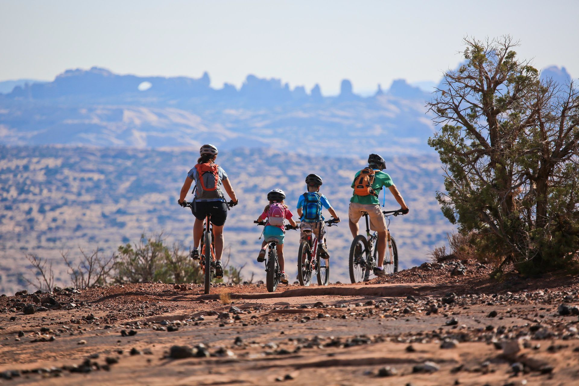 A family rides on the Moab Brand Trails with Arches National Park in the distance.