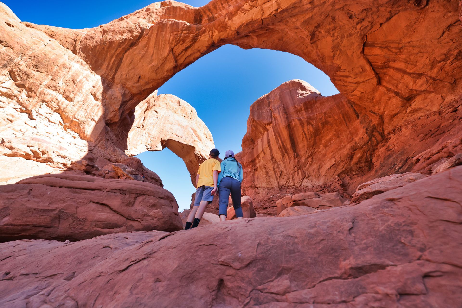 Hikers look up at Double O Arch in Arches National Park.
