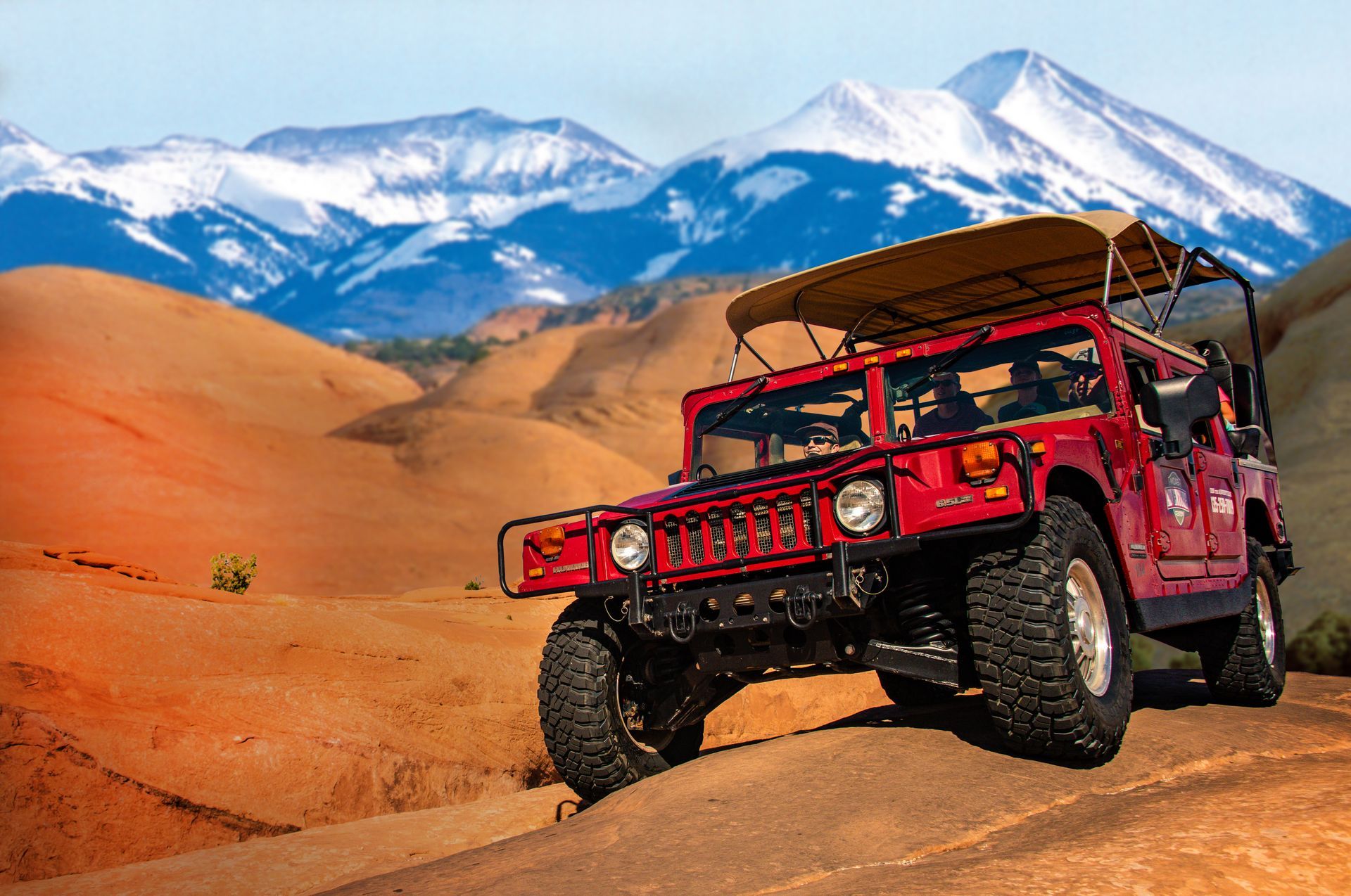 Red Hummer on a dirt path in front of mountains with snow-capped peaks.