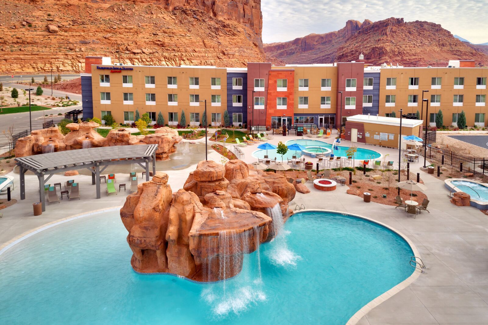 Hotel with multiple pools, water features, and red rock backdrop.