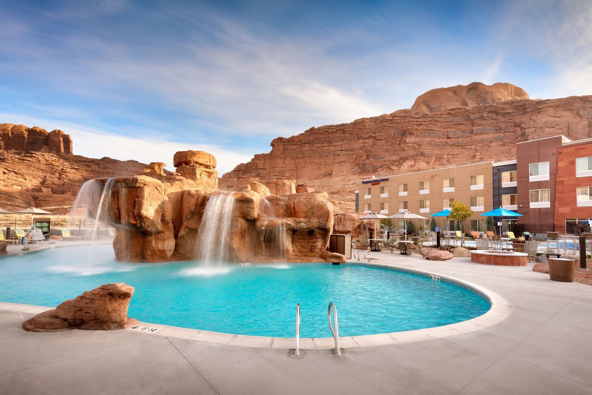 Pool with waterfall feature at a resort in front of red rock mountains.