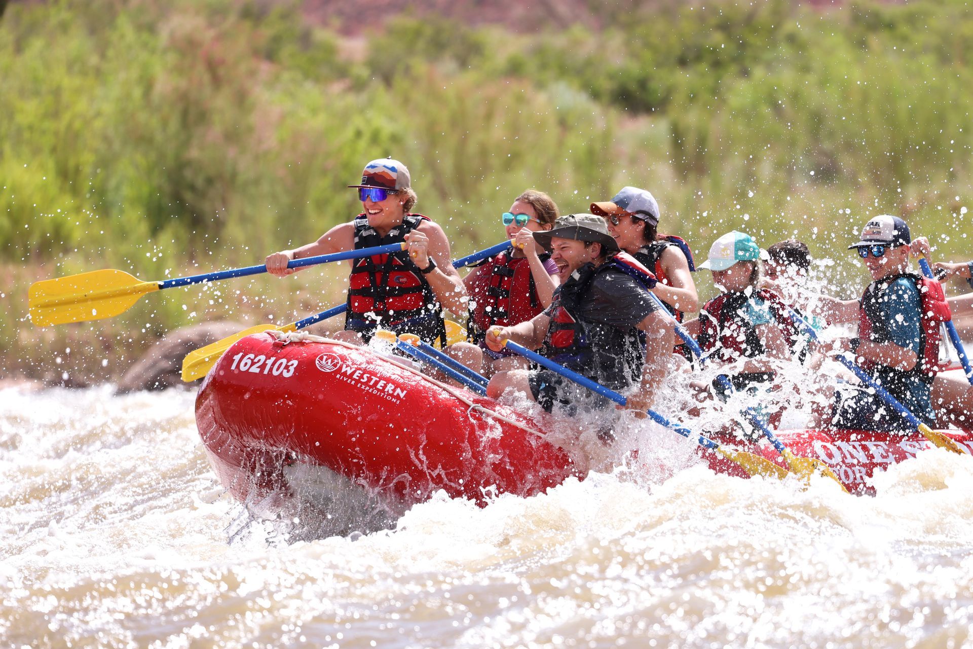 People white water rafting in a red raft on a rushing river, paddling through the rapids.