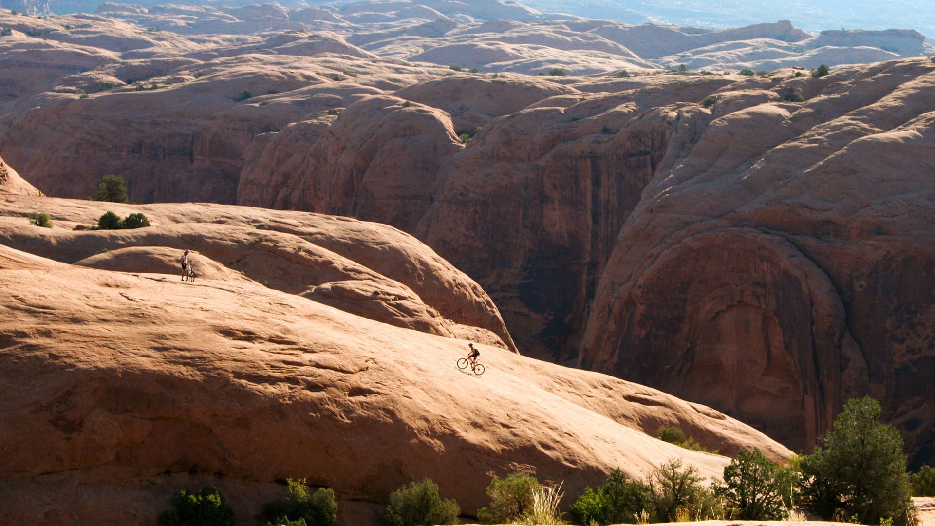 Mountain biker on a slickrock trail, Moab, Utah. Sunlit landscape with red rock formations.