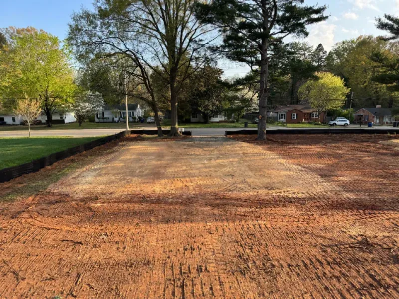 Freshly graded dirt lot with trees and a grassy park in the background