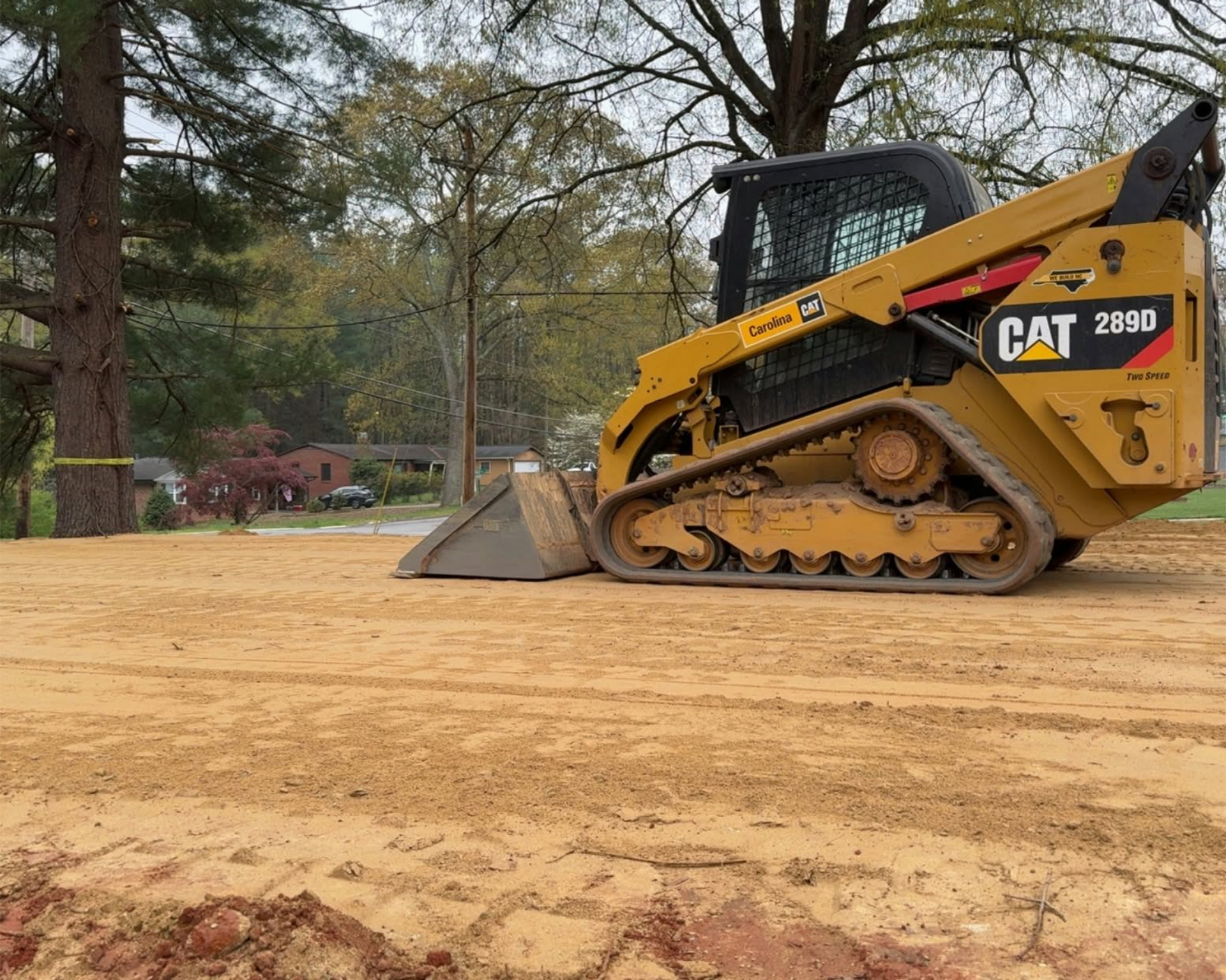 Yellow CAT mini excavator on a dirt lot with trees in the background