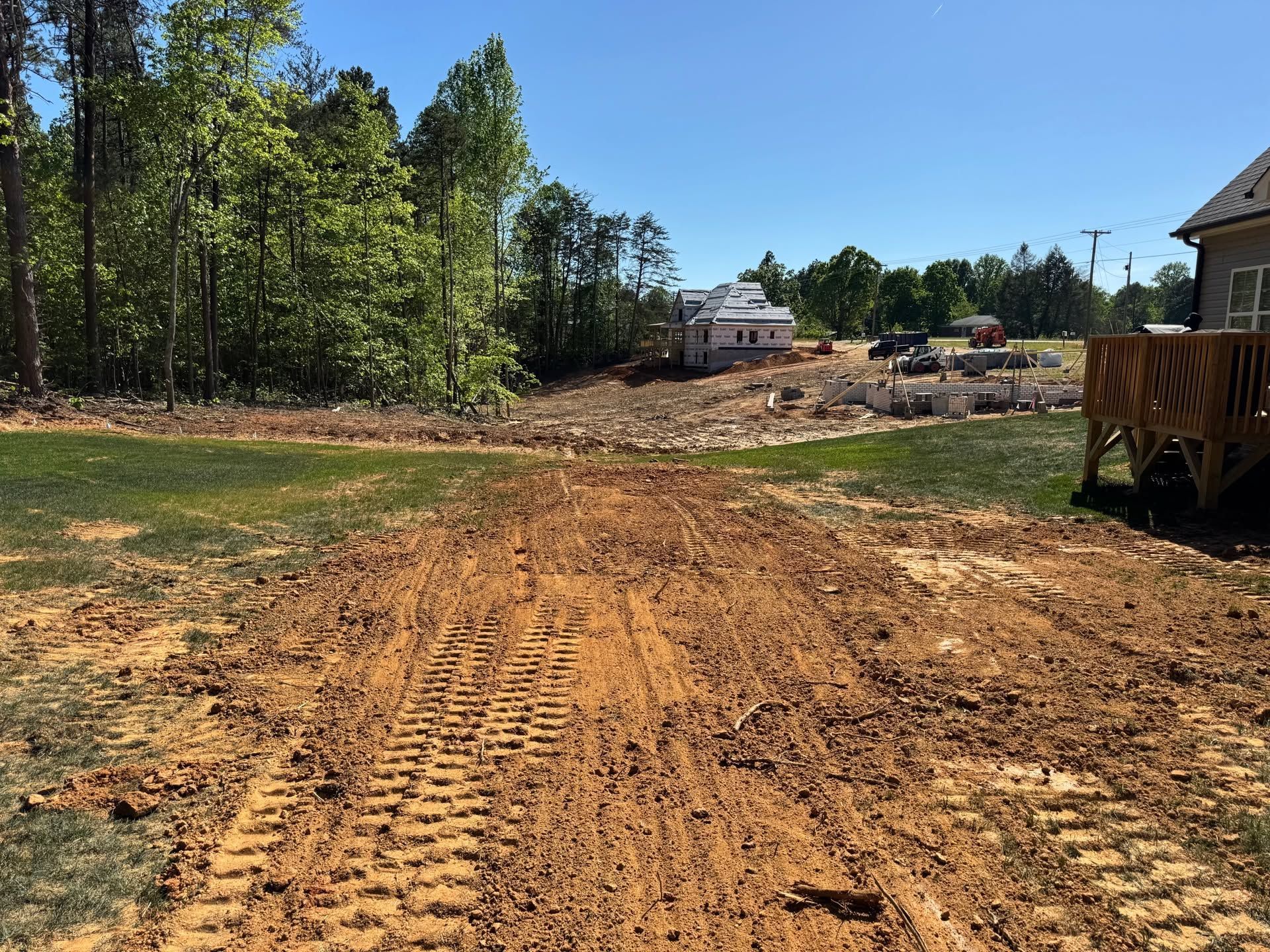 Freshly graded dirt road at a construction site with trees and houses in the background