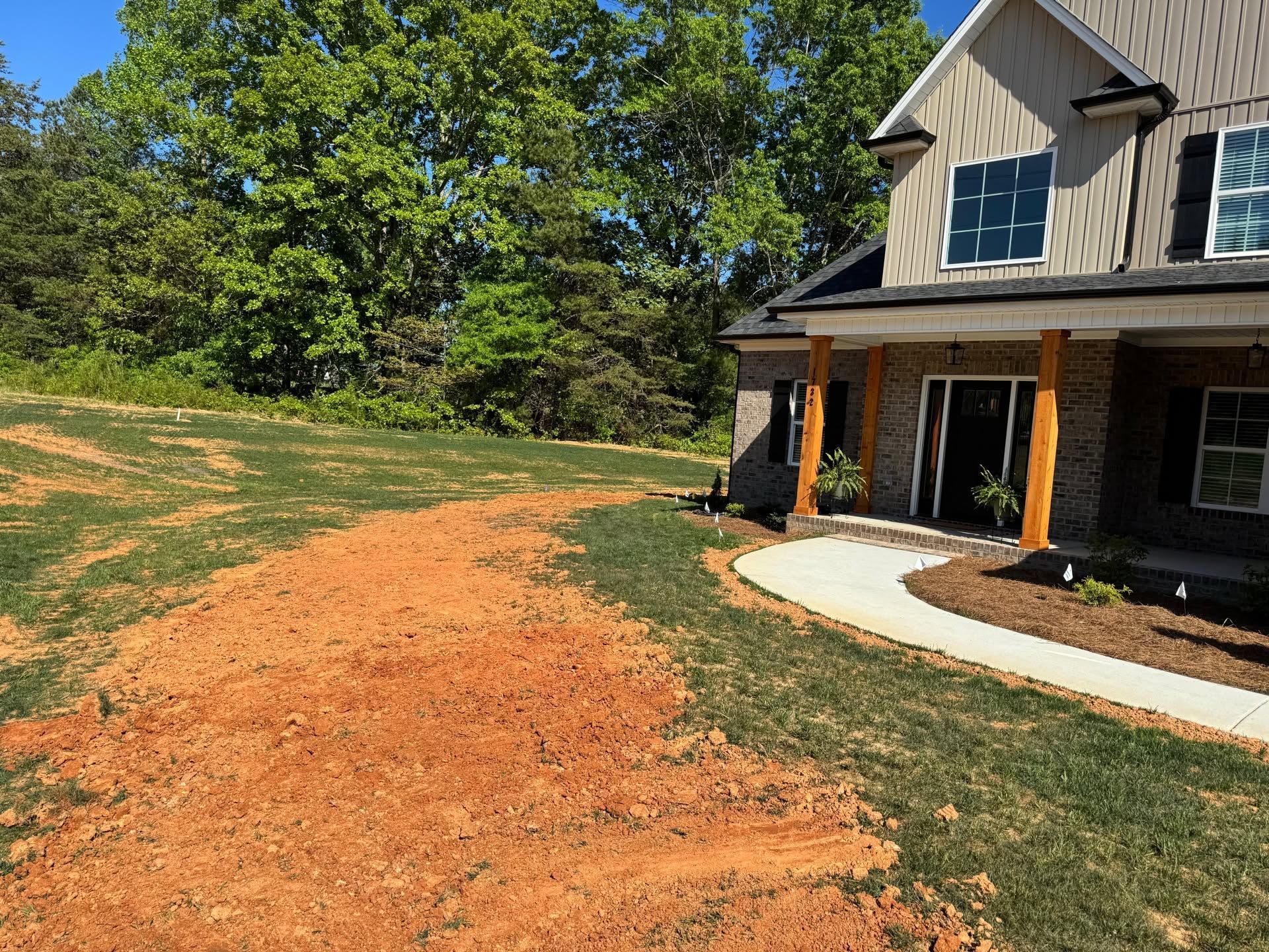 Curved gravel walkway beside a house with porch, lawn, and trees on a sunny day