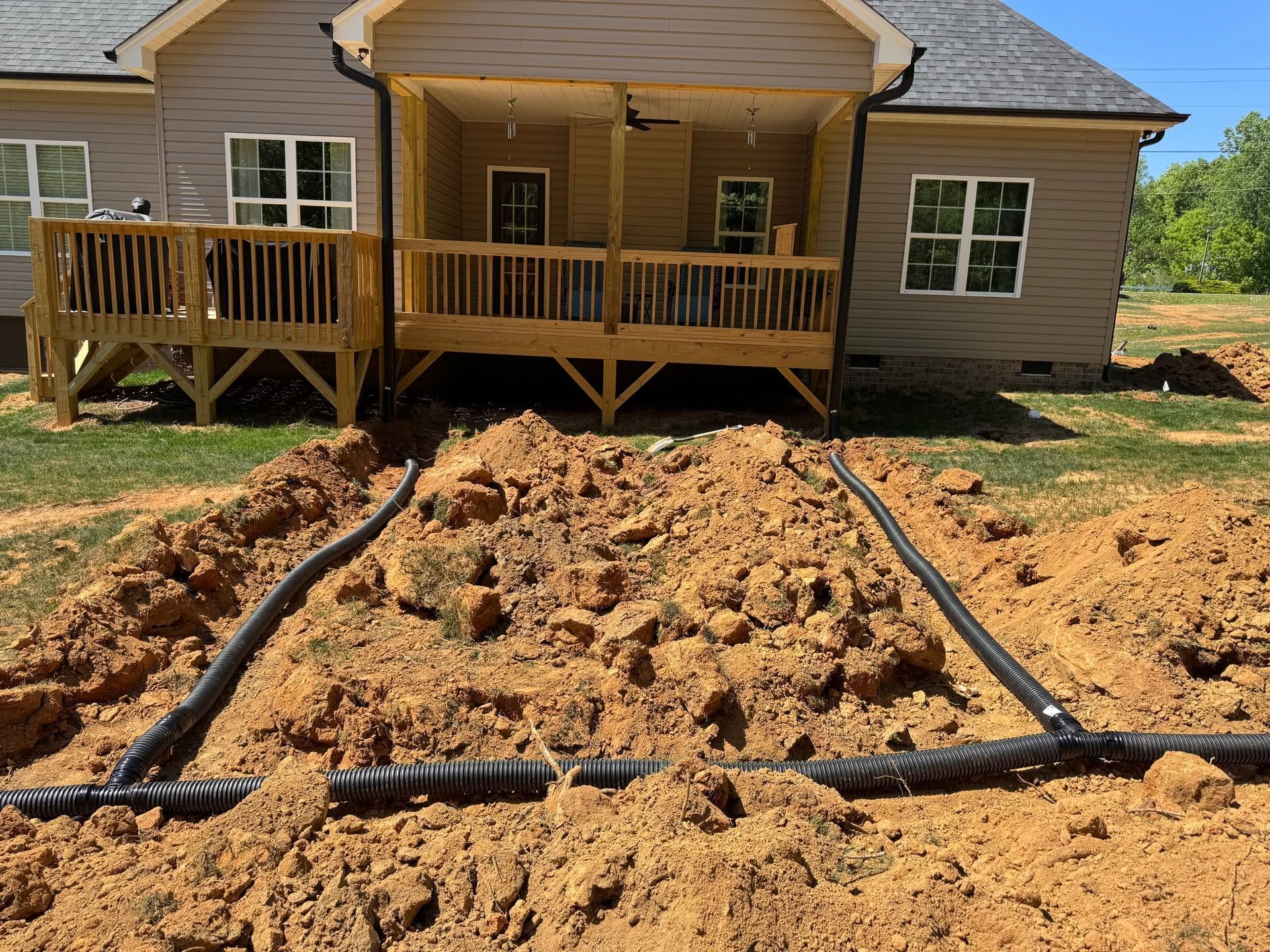 House with damaged front yard and exposed soil after construction, with black drainage pipes in the foreground
