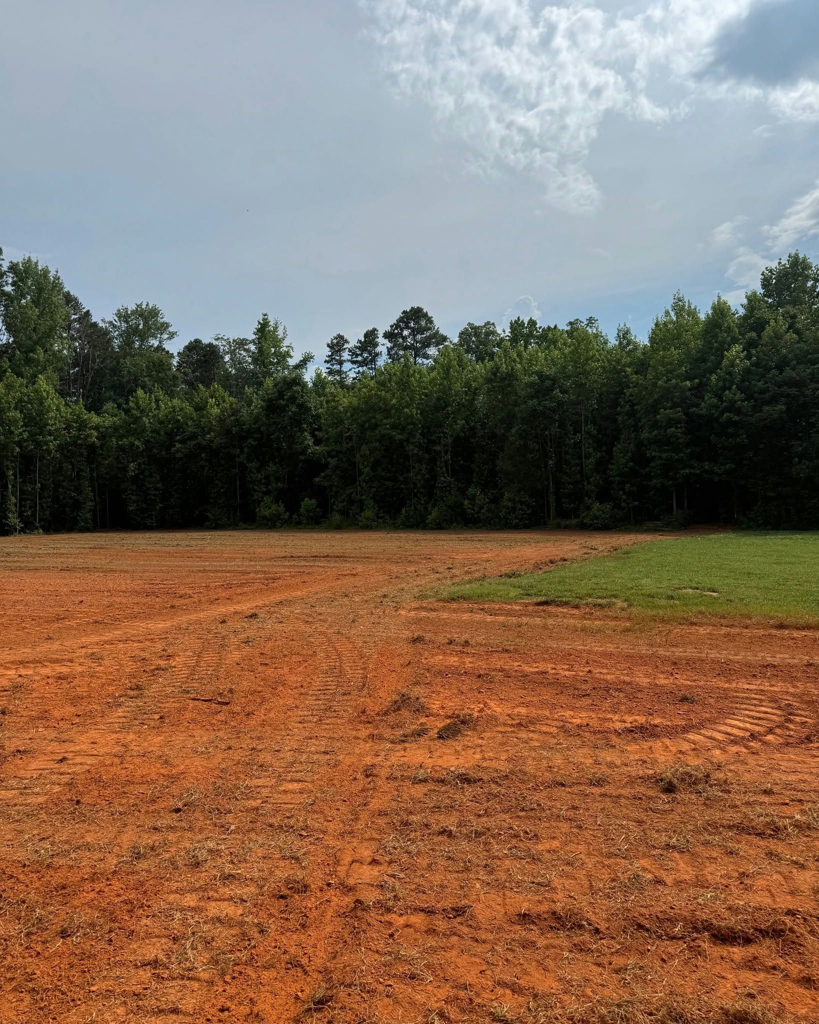 Open dirt clearing bordered by trees under a cloudy sky