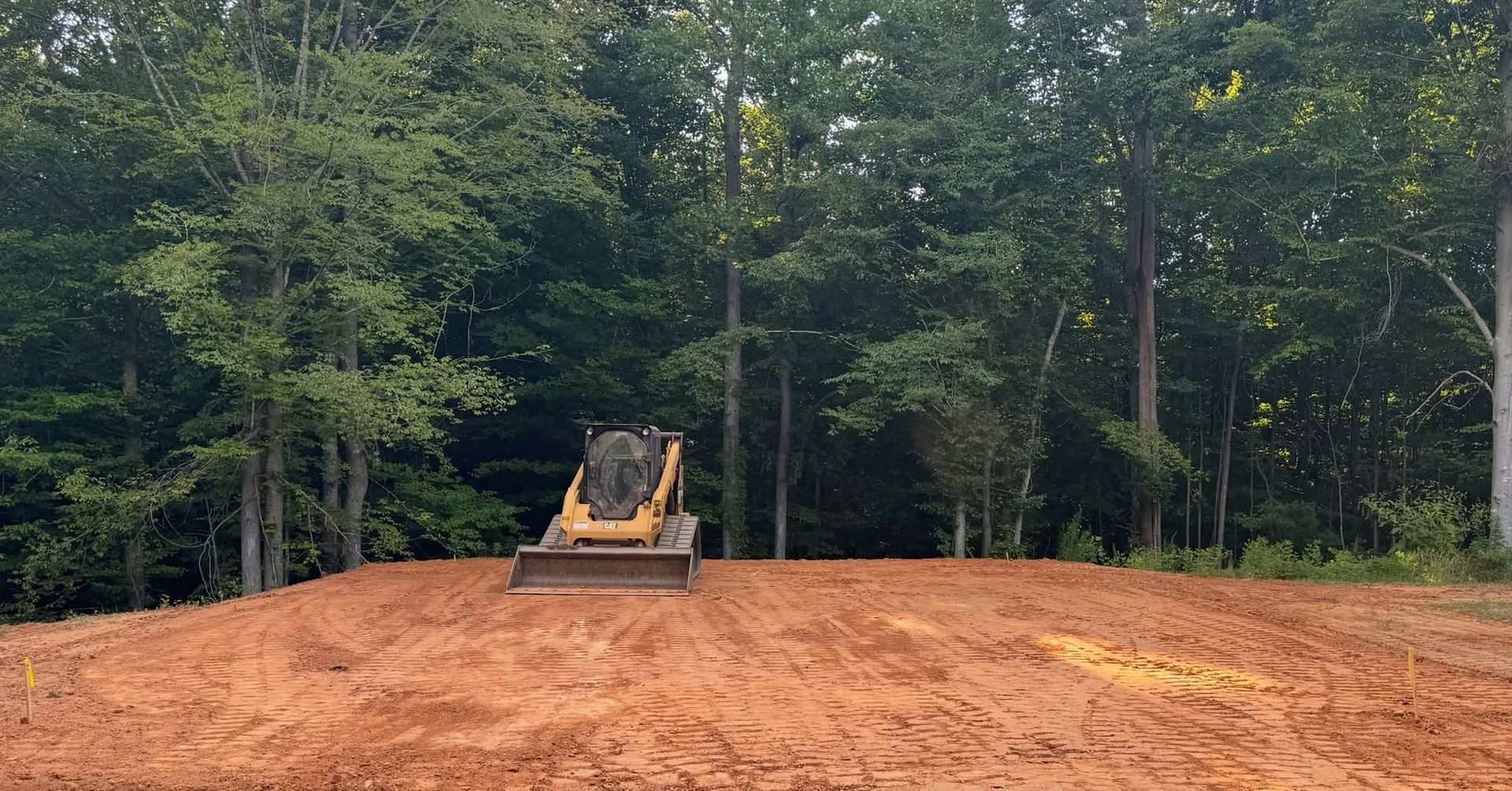 Bulldozer leveling a red dirt clearing at the edge of a wooded area