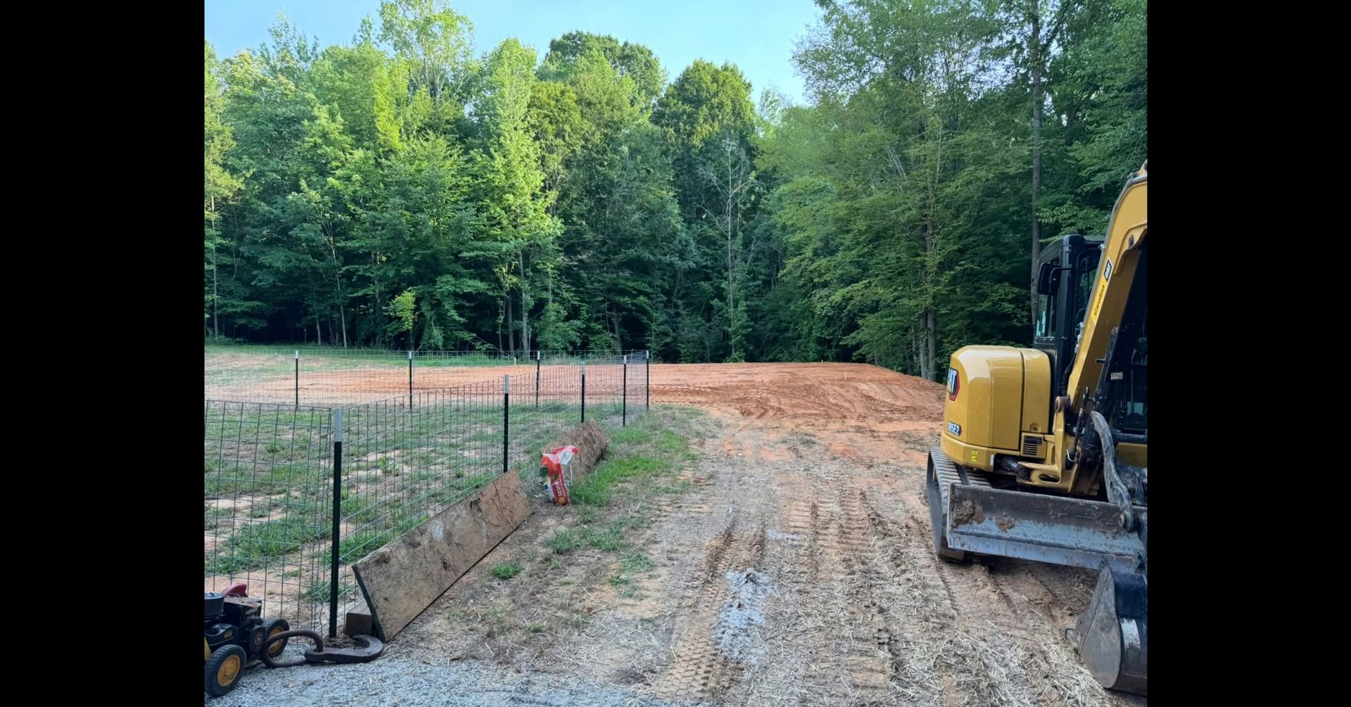 Gravel driveway under construction beside trees, with a yellow excavator and dirt grading area.