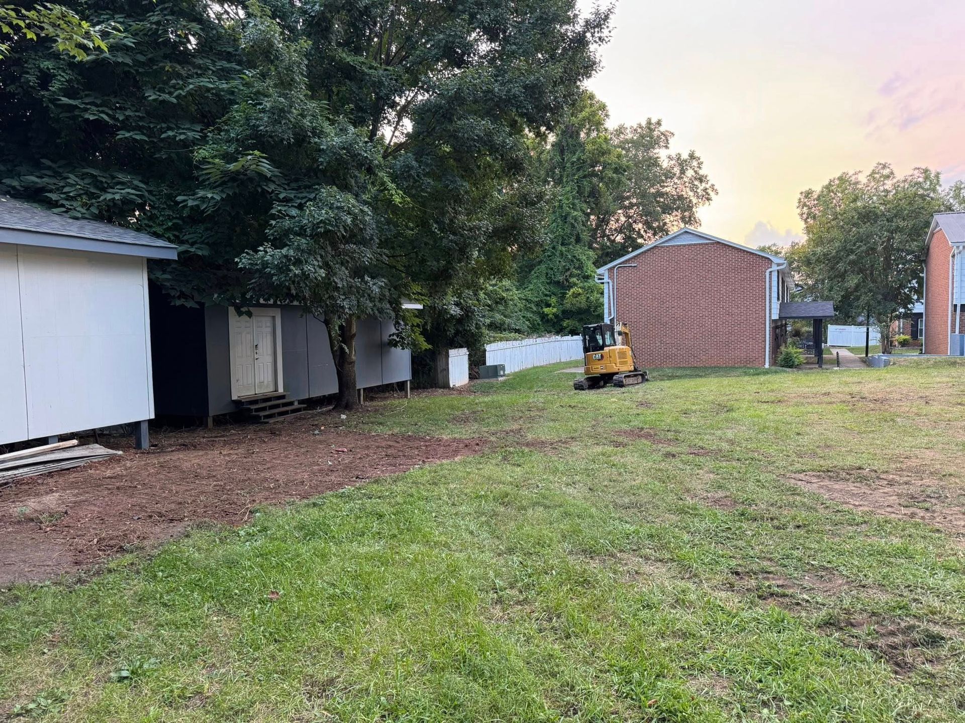 Grassy yard with trees, a white shed, and a small red shed at sunset
