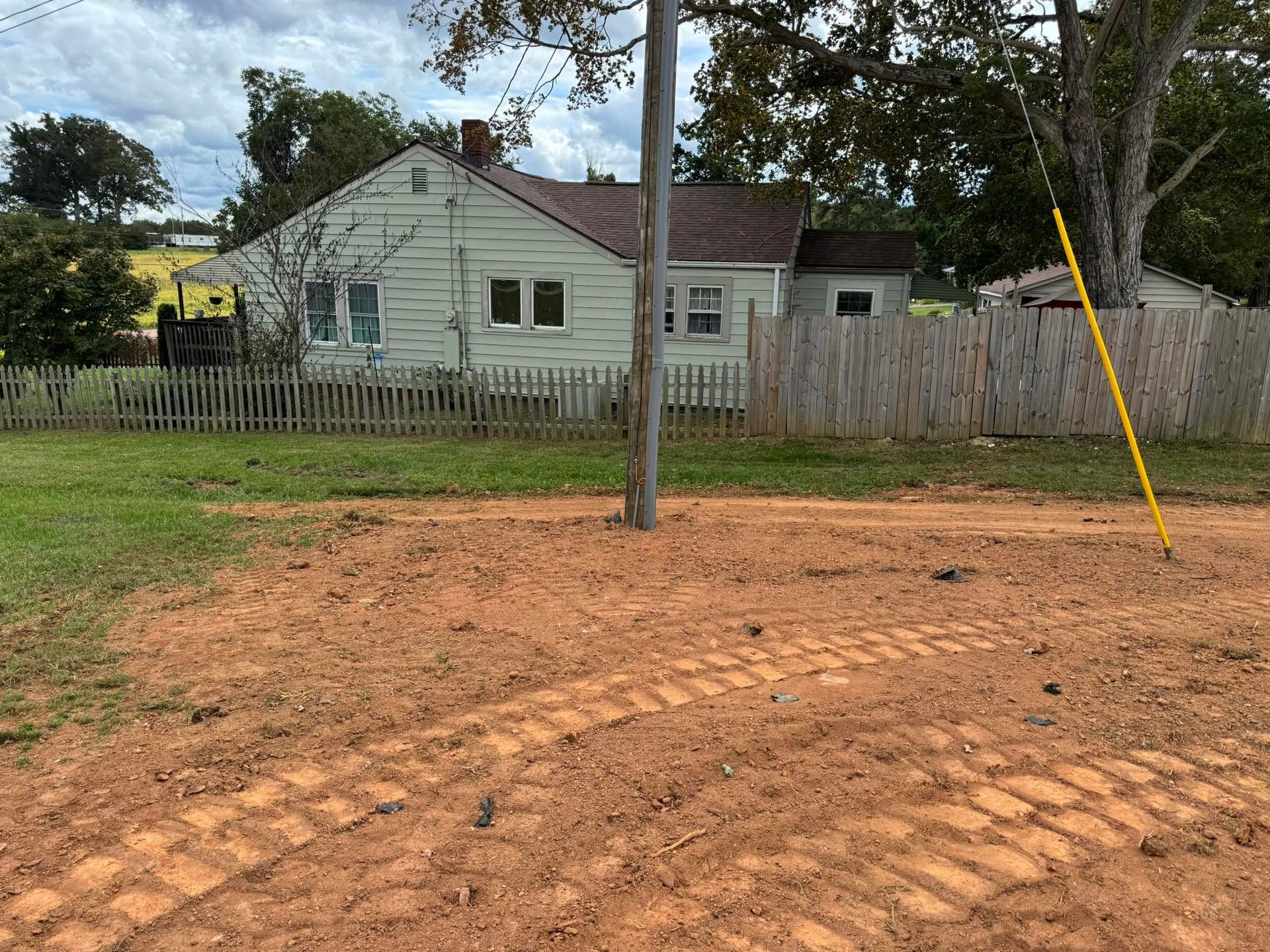Small white house behind a wooden fence, with a dirt lot and utility pole in the foreground.