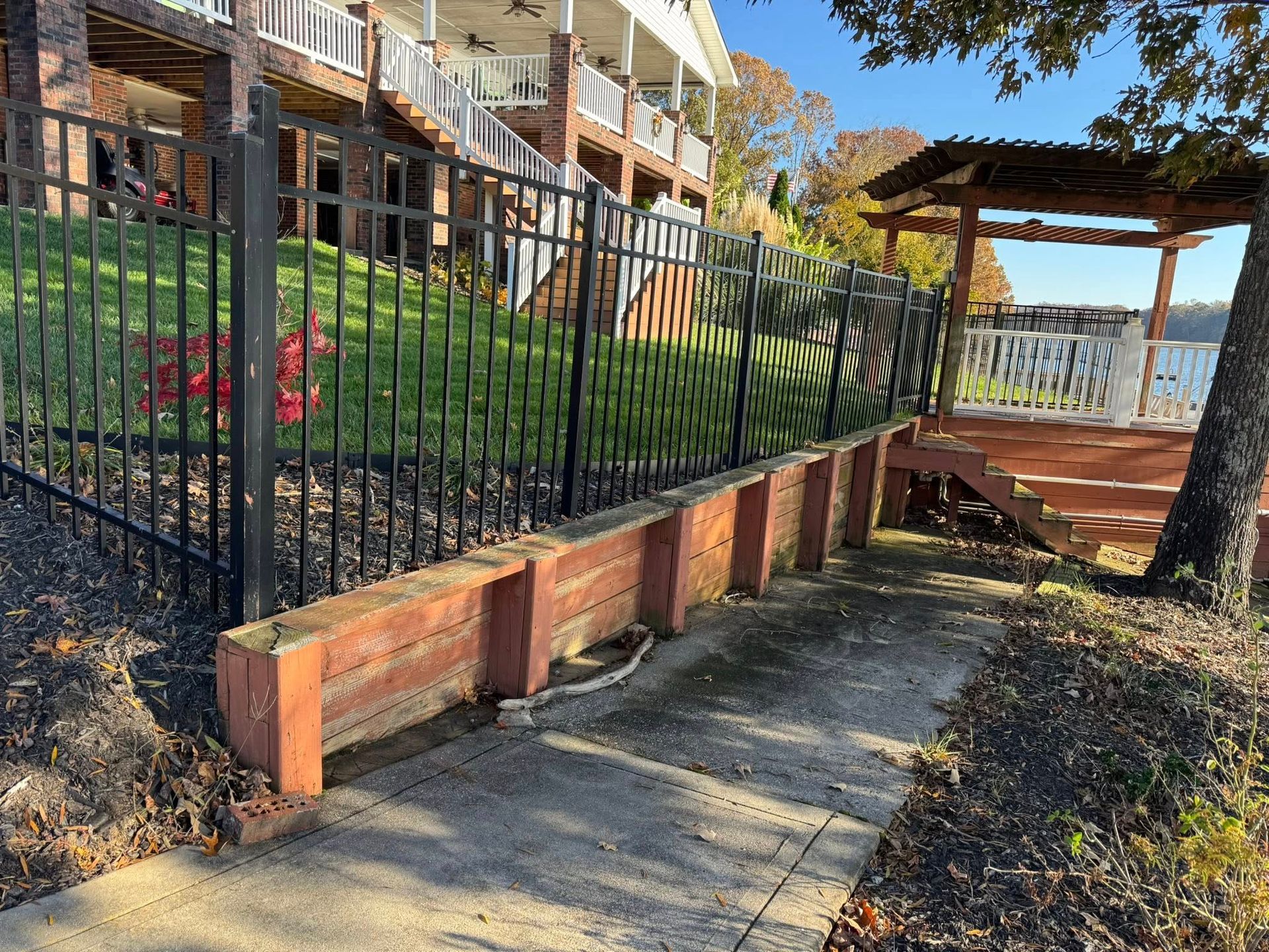 Brick retaining wall beside a fenced garden path leading to a wooden pergola and water view