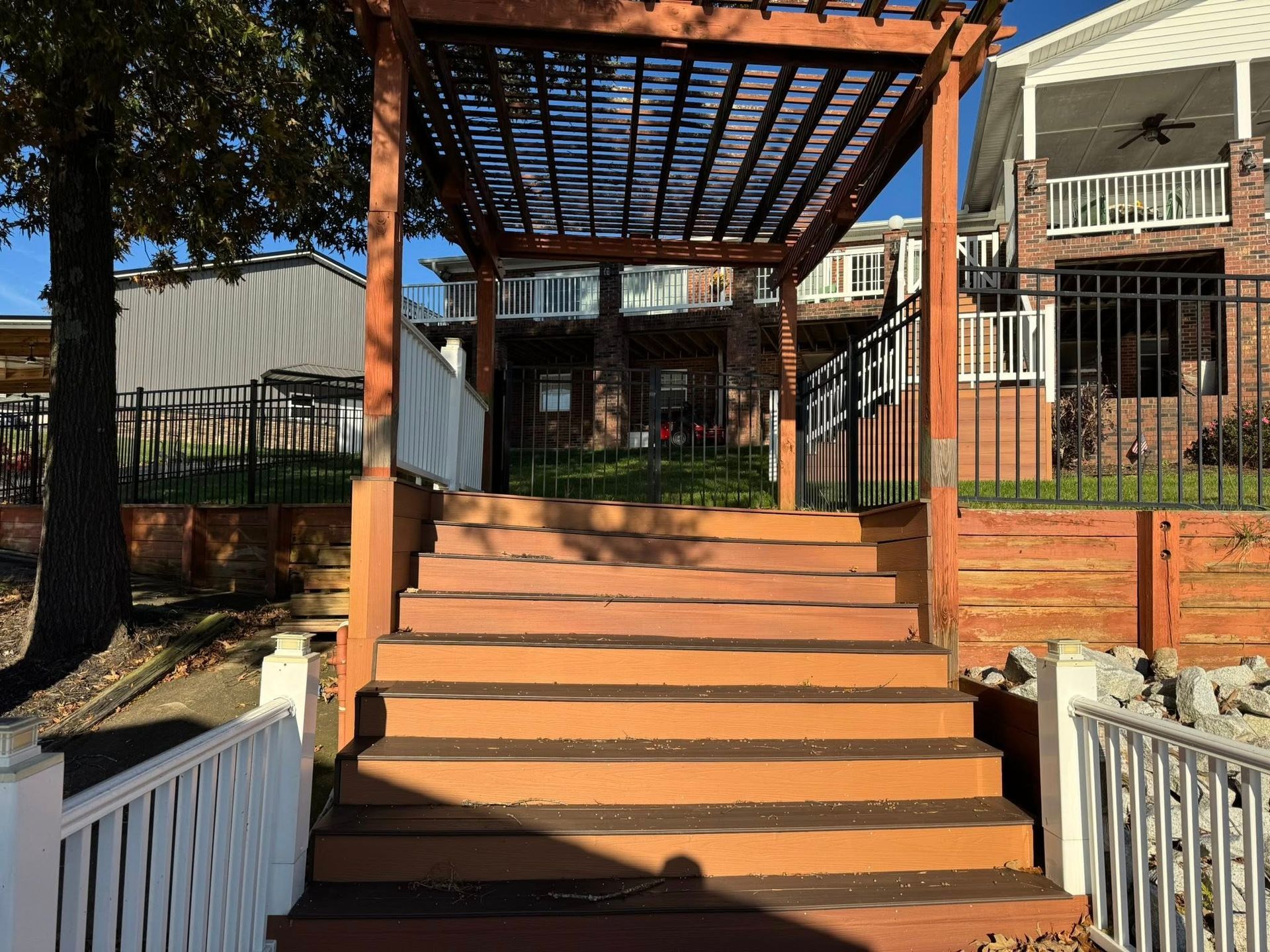 Wooden stairs with a pergola leading to a brick building entrance, framed by white railings.