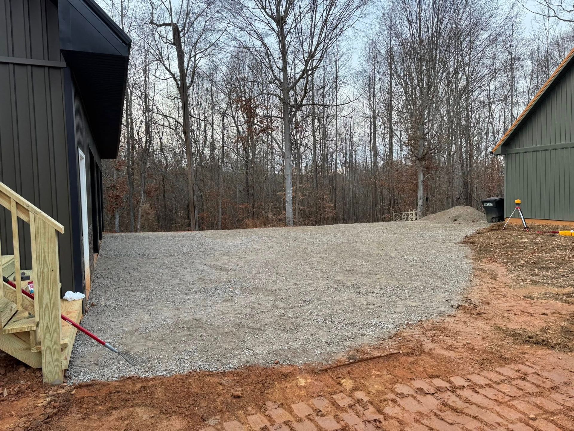 Gravel driveway between two buildings, with a wooden deck on the left and bare trees in the background