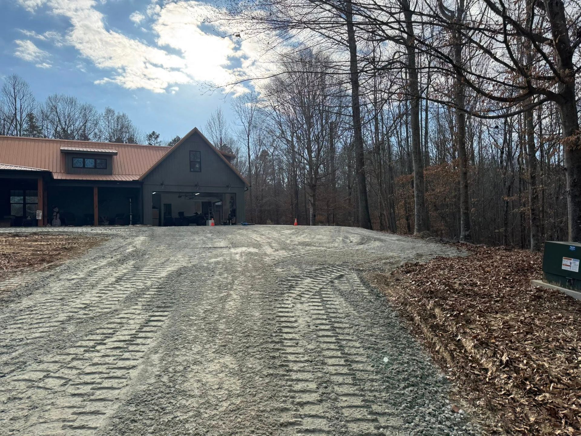 Gravel driveway leading to a house in a wooded yard under a cloudy sky