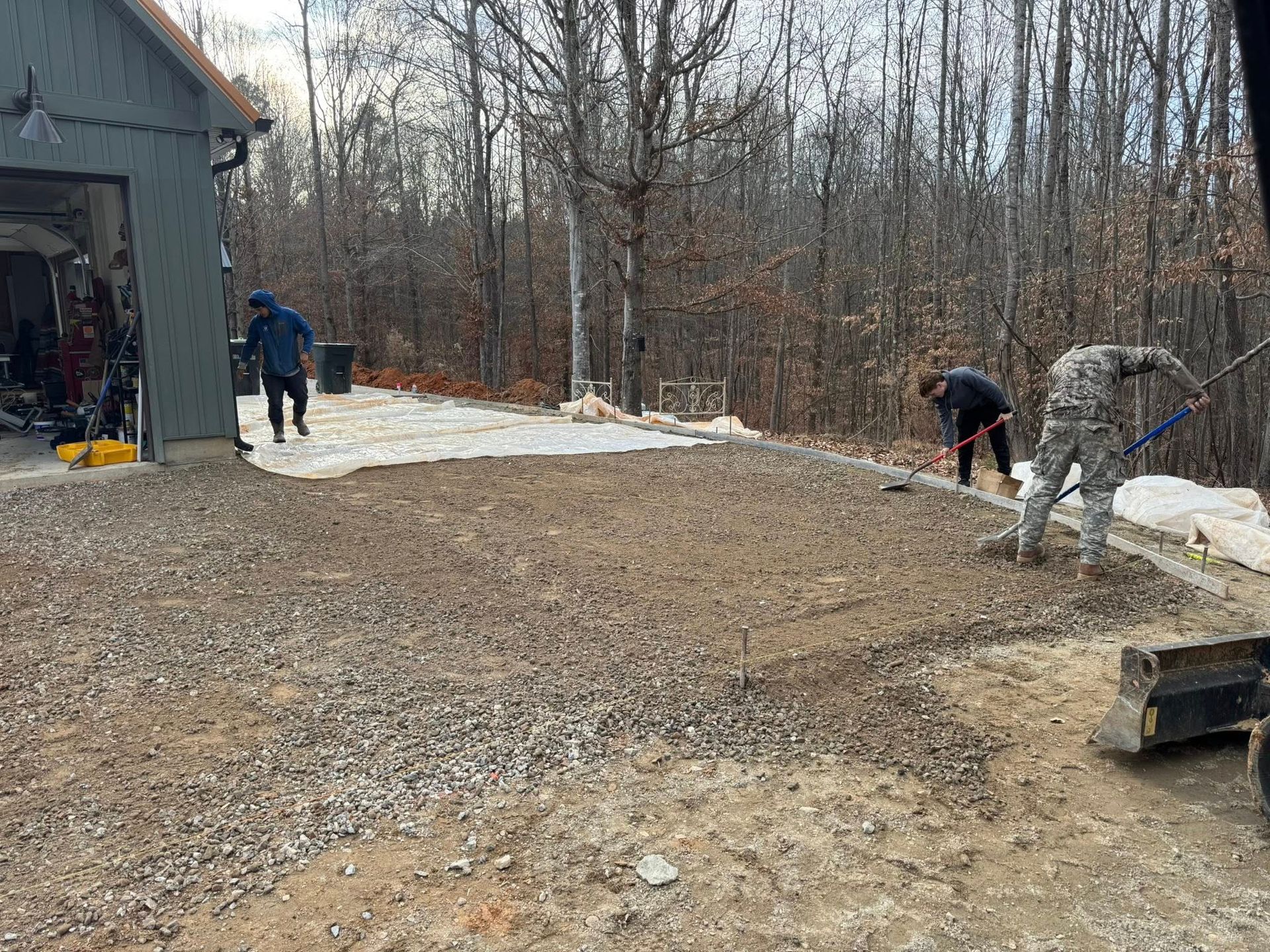 Workers spreading gravel beside a house on a snowy driveway
