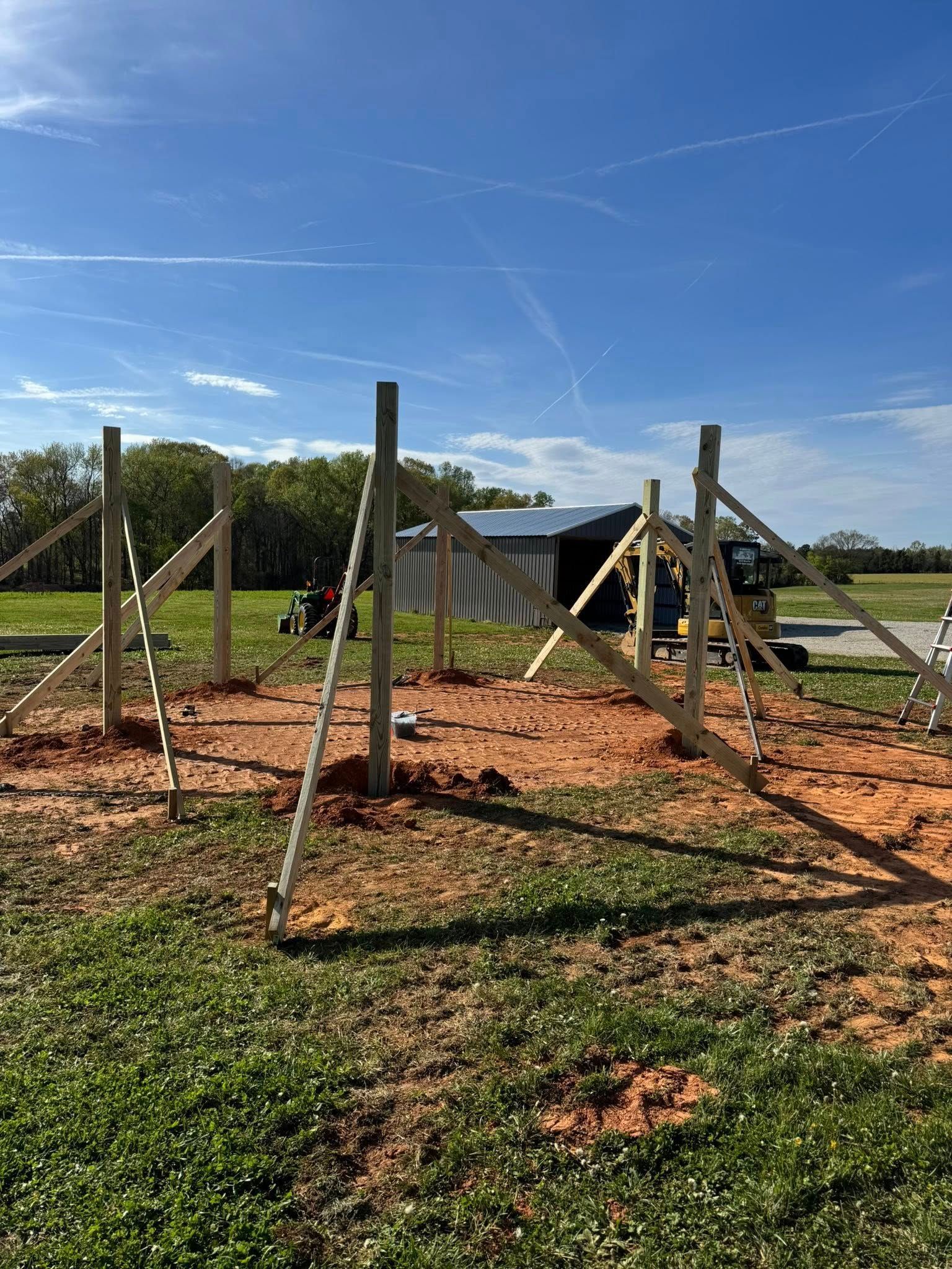 Wooden fence posts and braces in a grassy field under a clear blue sky