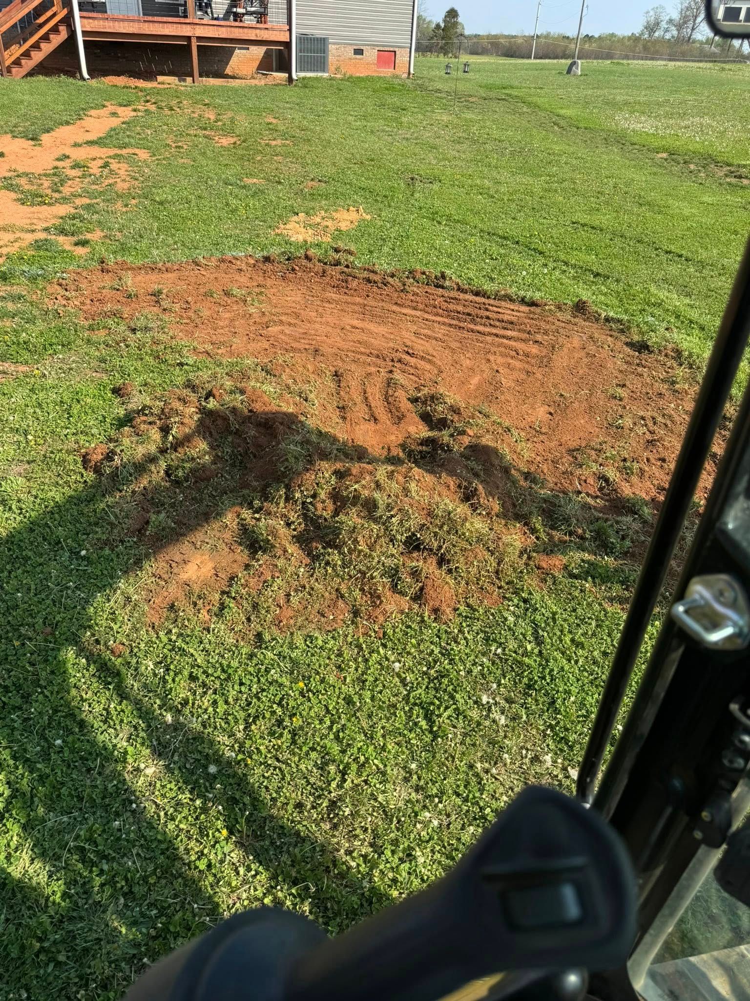 Large dirt patch on green grass near a vehicle and farm equipment outdoors