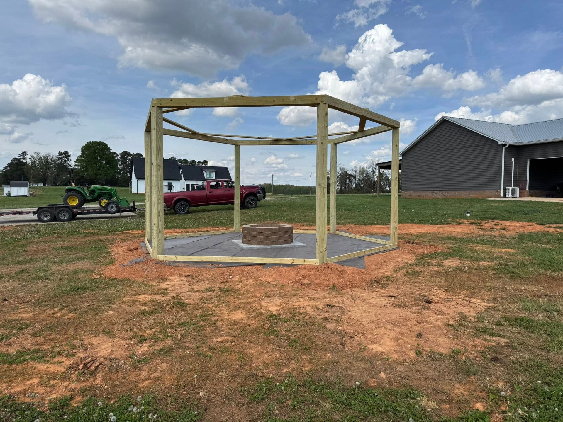Wooden shelter frame on a concrete pad at a construction site, with a red truck and house nearby.