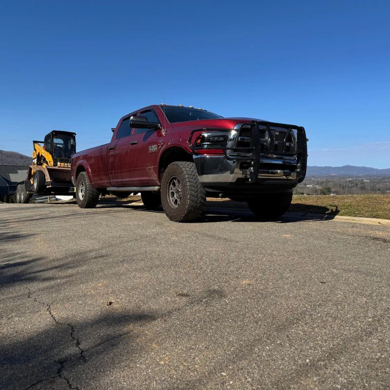 Red pickup truck towing a yellow off-road vehicle on a rural road under a clear blue sky