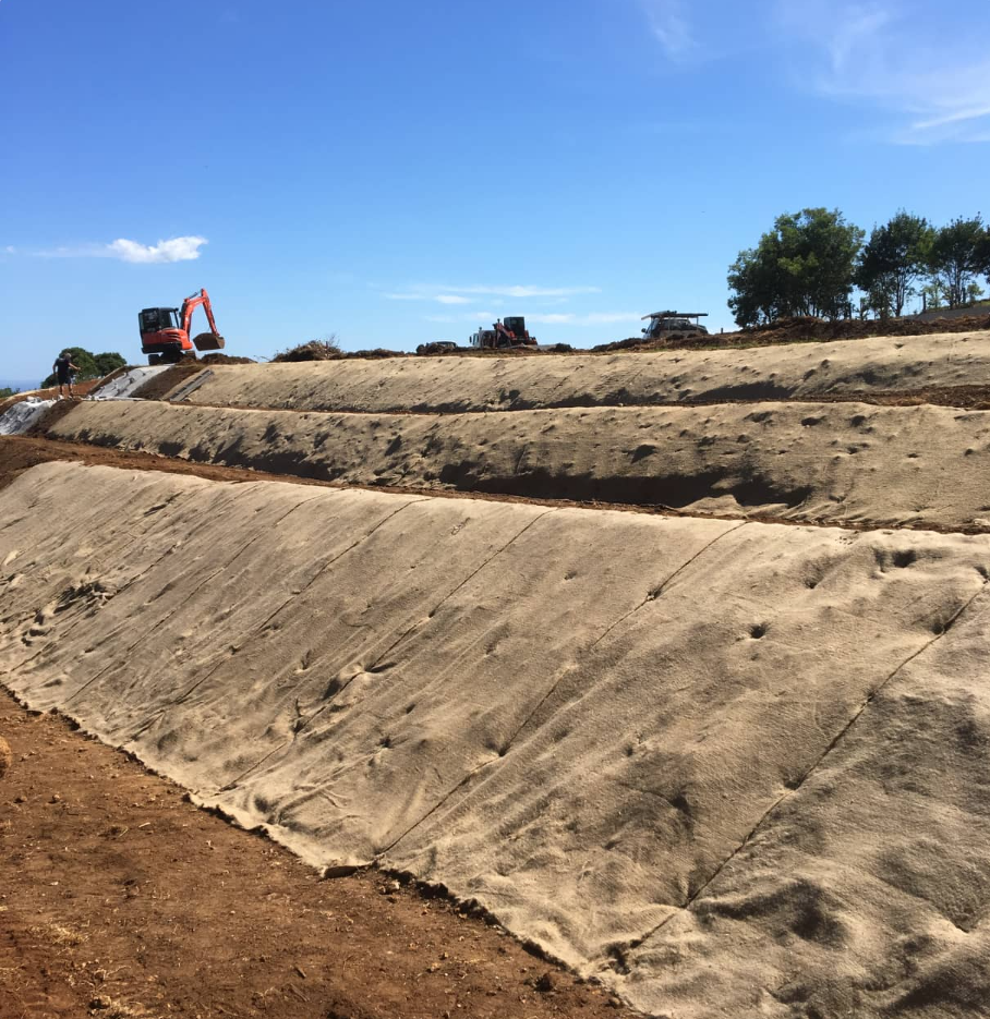 Excavator grading a dirt slope under a clear blue sky.