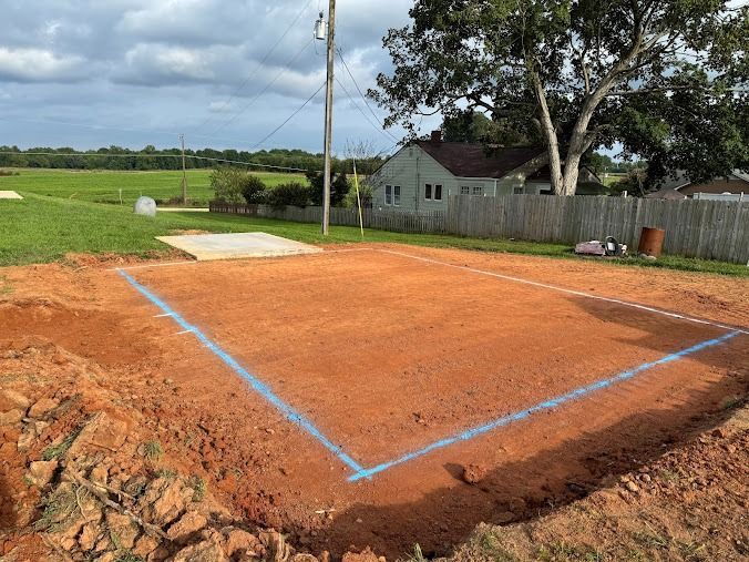 Bulldozer grading red dirt lot with a yellow container and trees in the background