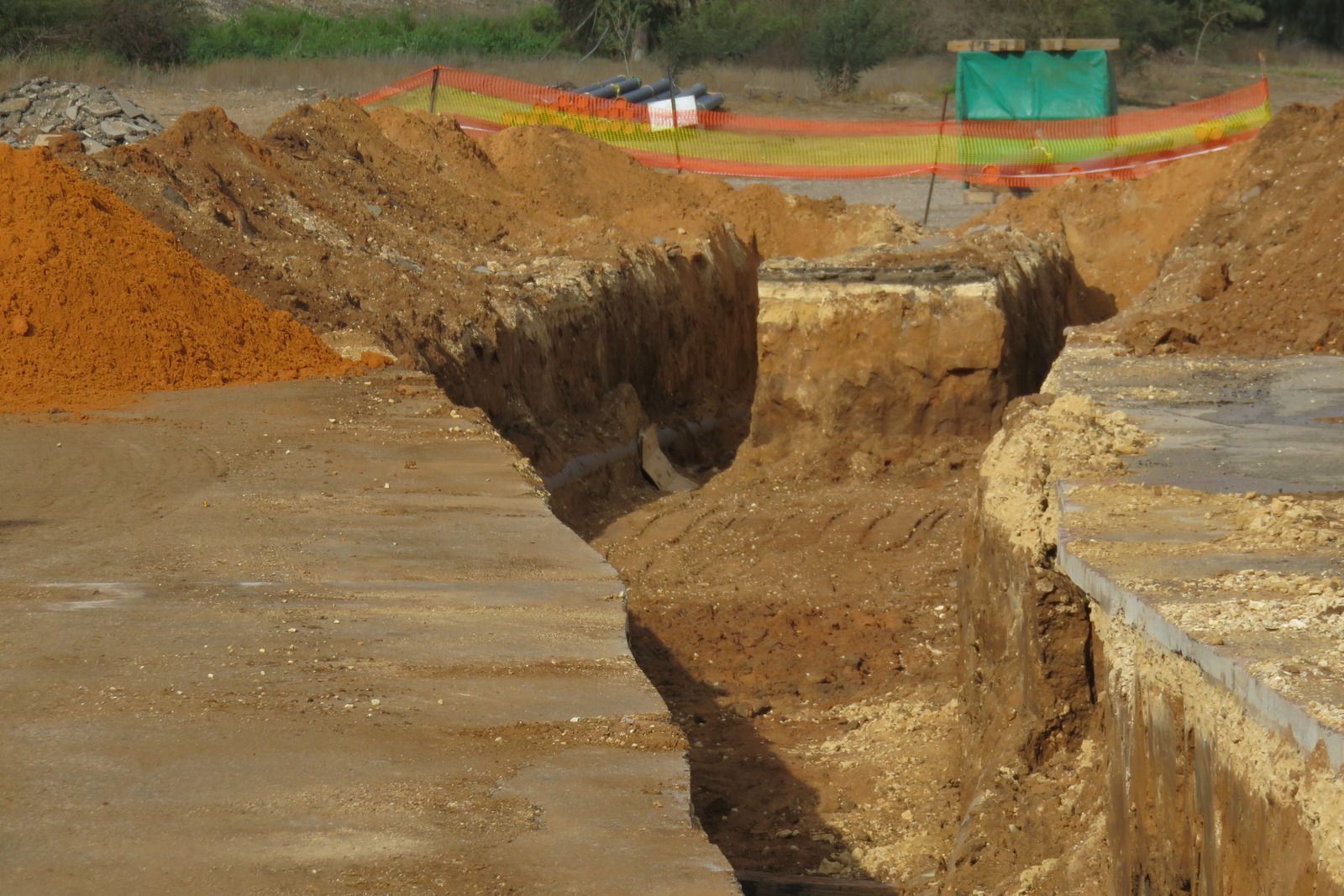 Large eroded trench in a dirt construction site, with a steep collapse and orange safety fencing in the background