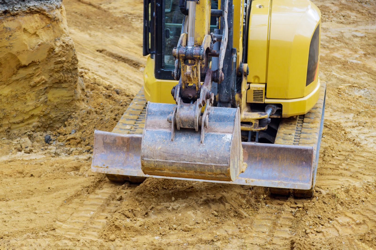 Yellow excavator bucket leveling dirt at a construction site