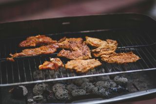 Chicken grilling on a barbecue, with seasoned pieces over hot charcoal flames