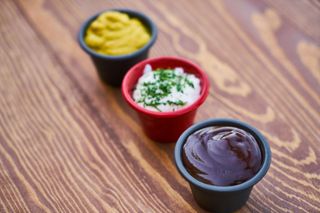Three small cups of chutney or dips on a wooden table, topped with herbs and spices