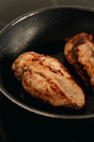 Two browned chicken breasts searing in a black skillet