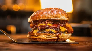 Stacked cheeseburger with melted cheese and bacon on a wooden table, warmly lit in a restaurant setting
