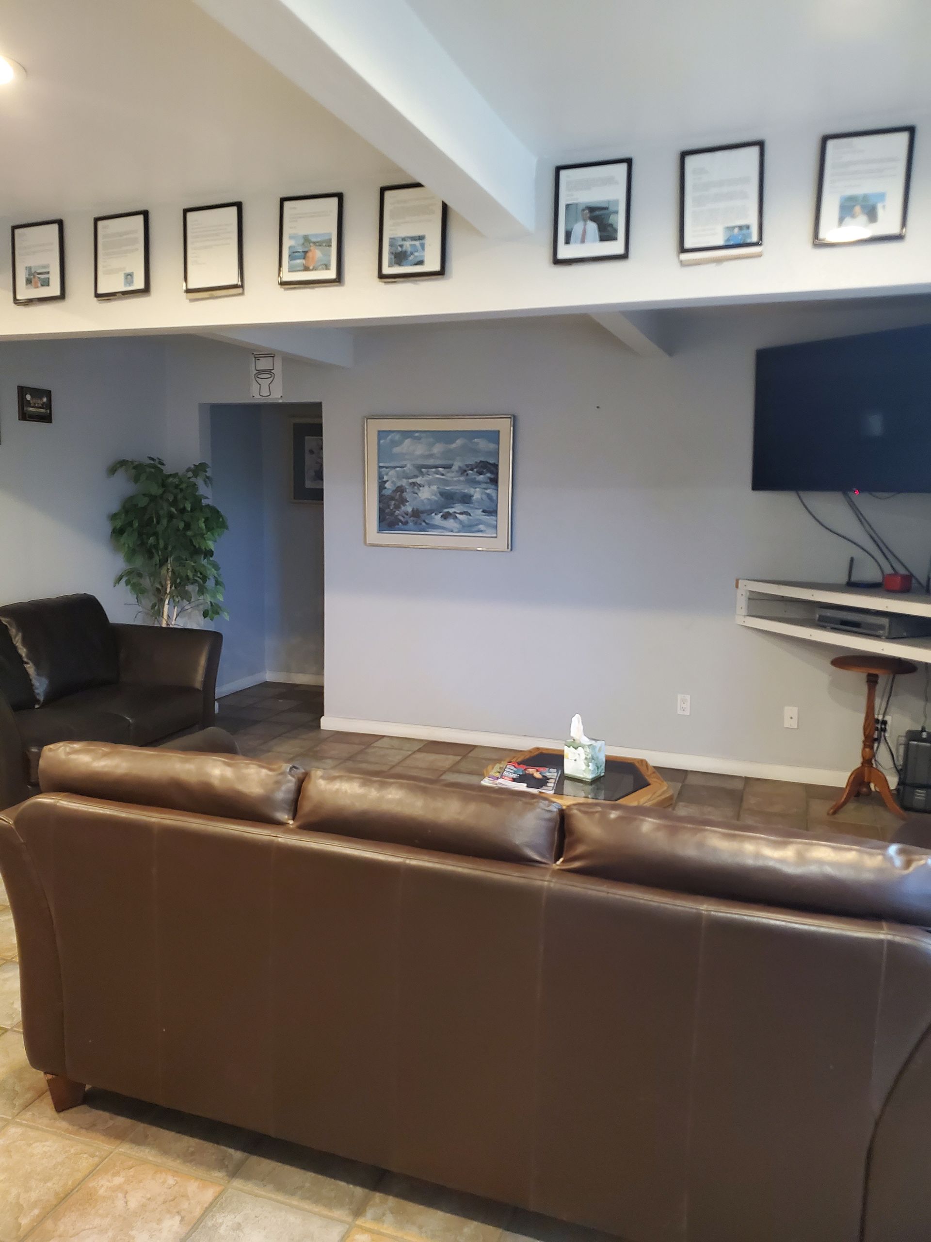 A living room with a brown leather sofa, framed photos, a TV, and a painting. | Hal's Auto Care