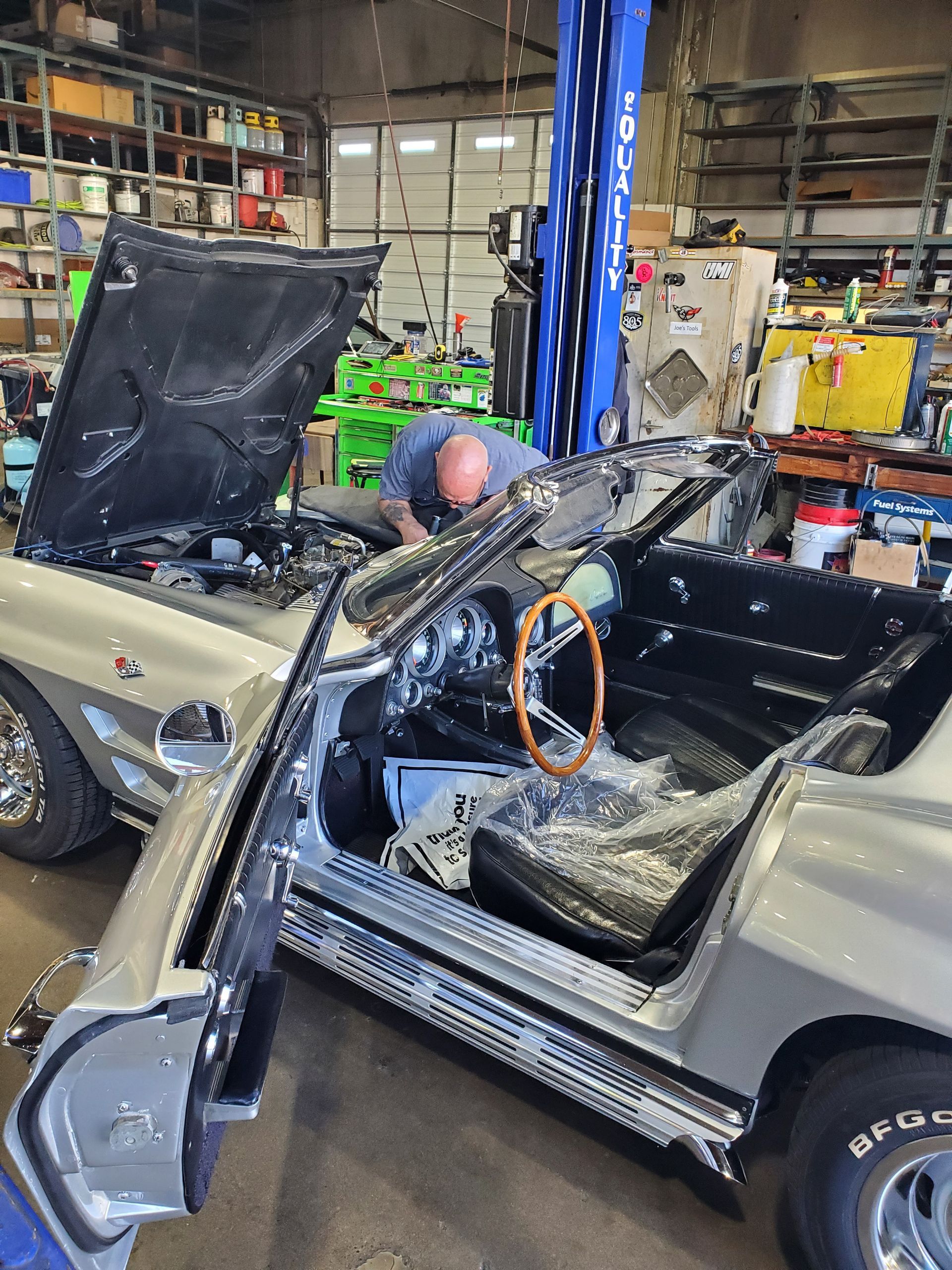 A mechanic working on a silver convertible in a garage. Open hood, door, and interior visible. | Hal's Auto Care