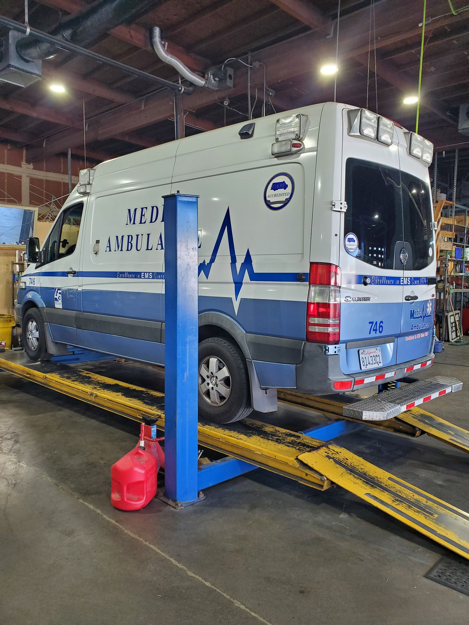 Ambulance on a lift in a repair shop; white and blue with GEORGIA AMBULANCE on the side. | Hal's Auto Care