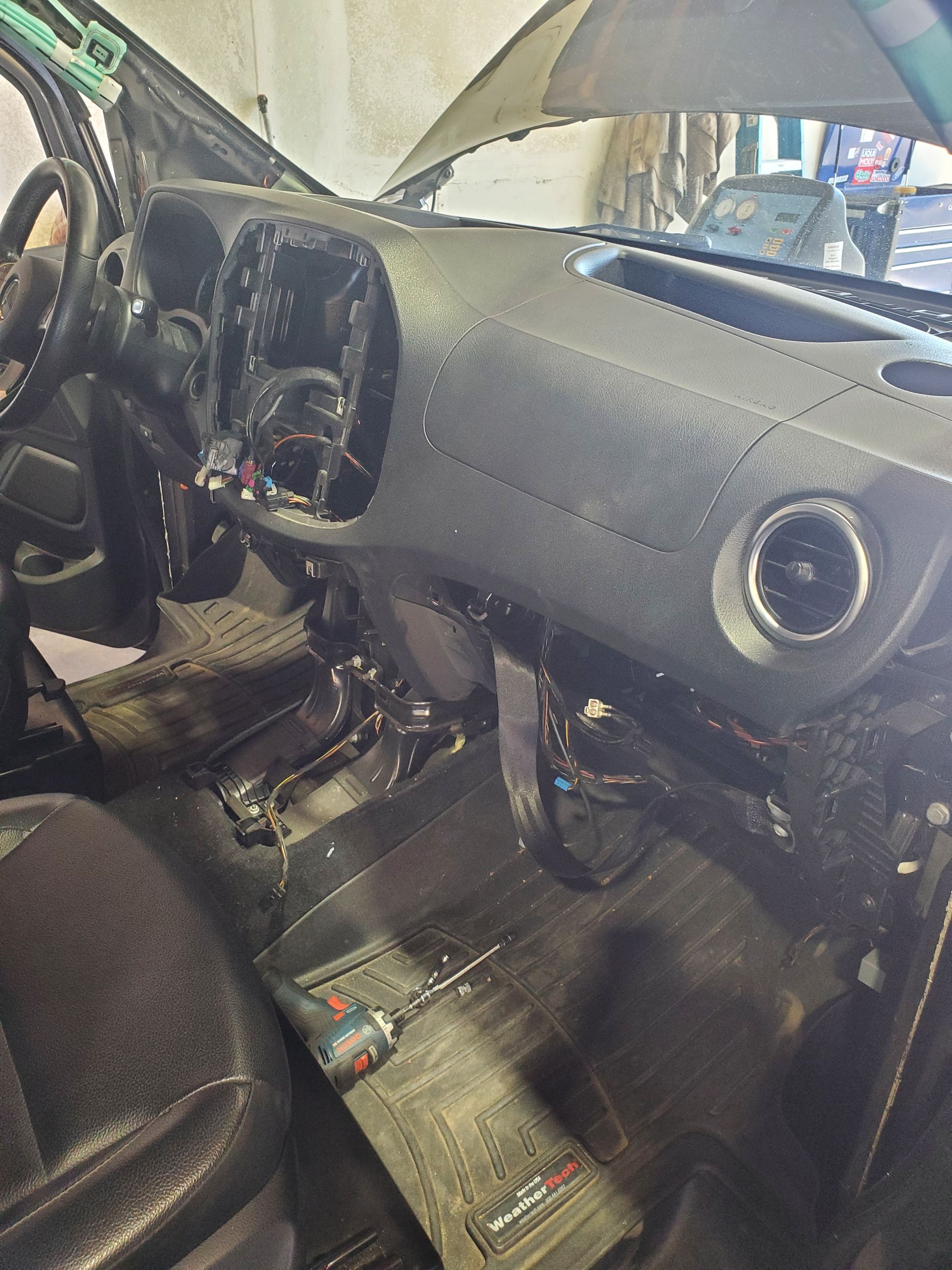 Interior of a van with dashboard partially disassembled, tools visible on the floor.