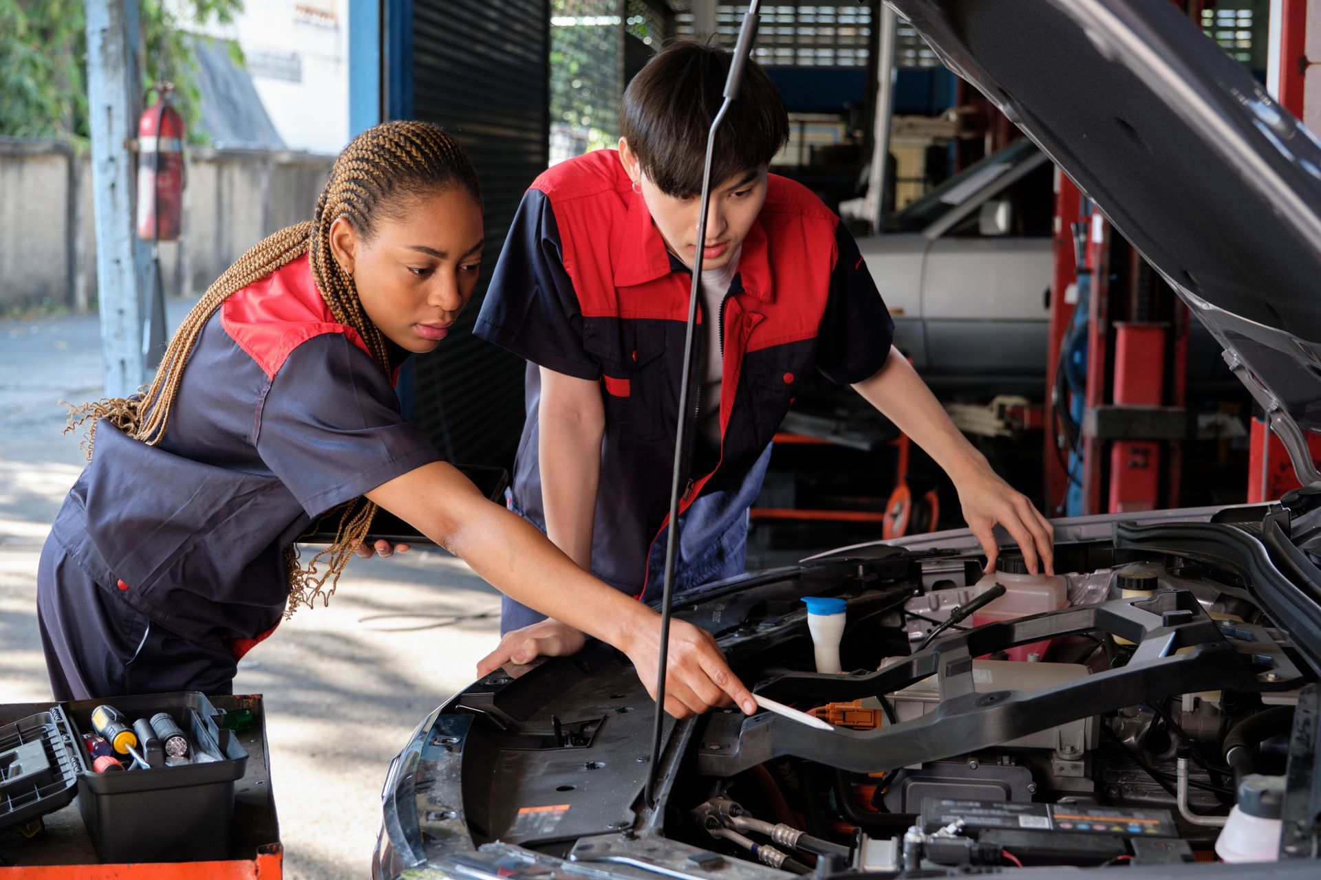 Two mechanics, a woman and a man, examining a car engine in a garage.