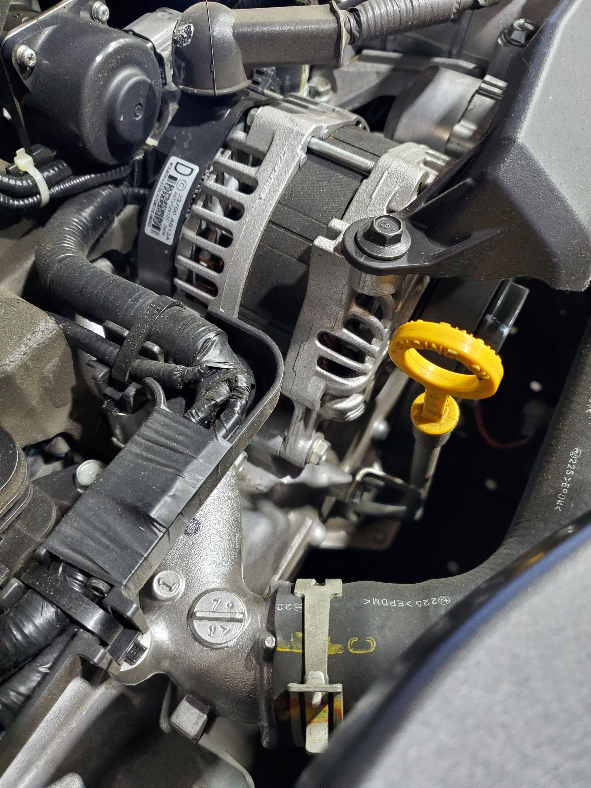 Engine bay with alternator and oil dipstick, with yellow handle.