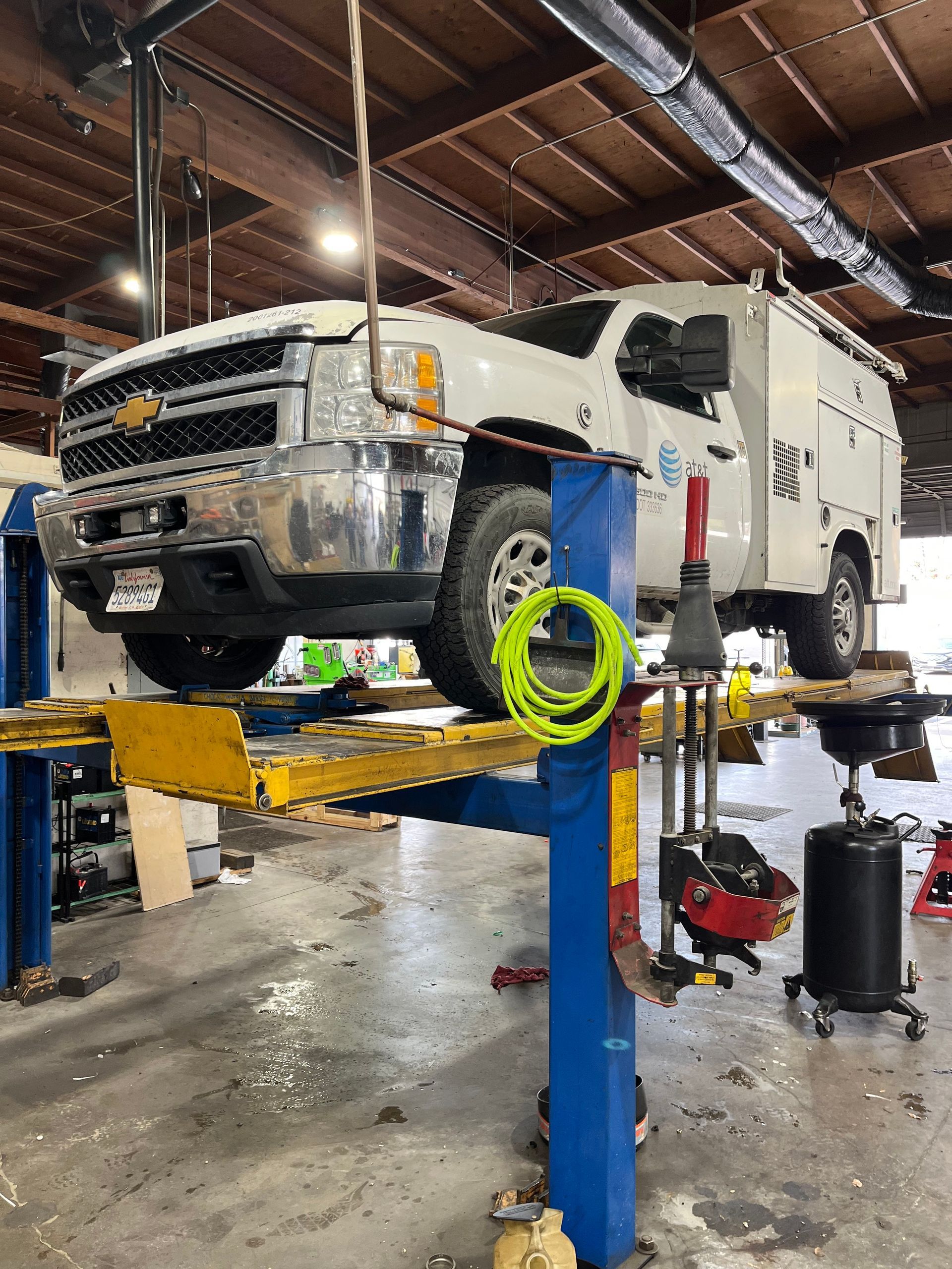 White Chevy truck on a blue car lift in a garage, being serviced. | Hal's Auto Care