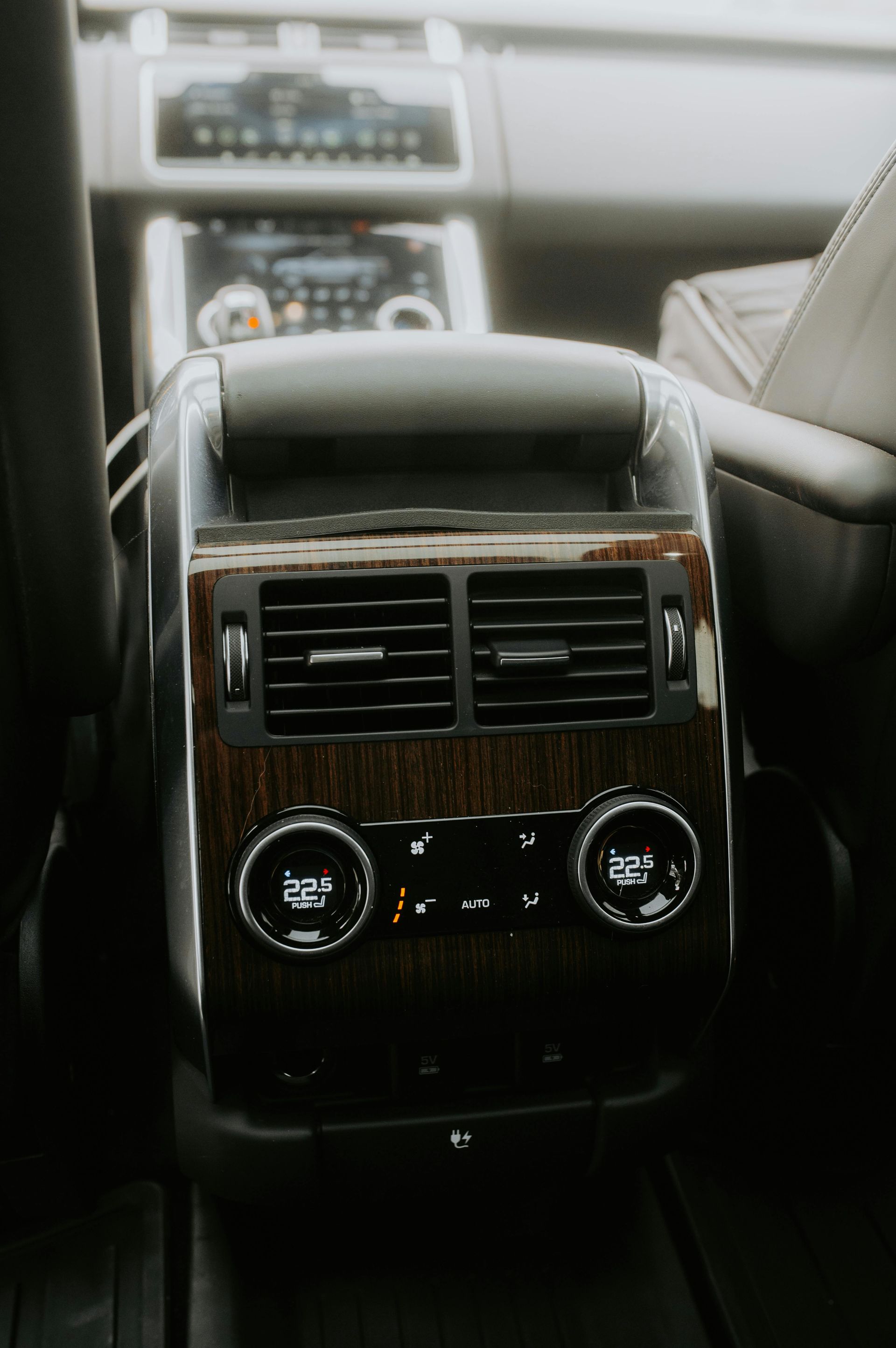 Car's rear console with wooden trim, air vents, and climate controls, in a blurred interior. | Hal's Auto Care