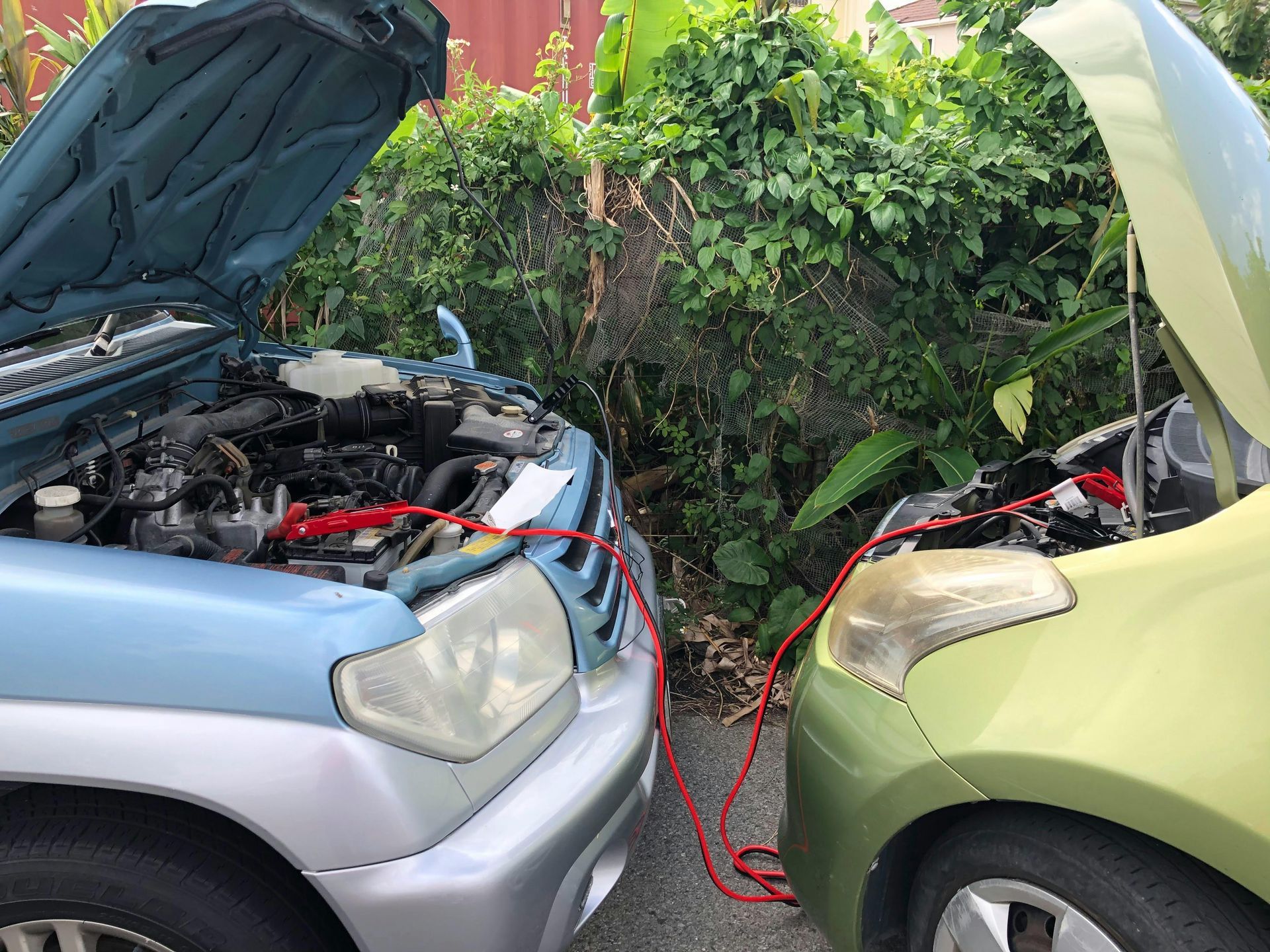 Two cars with open hoods connected by jumper cables; one blue, one green.