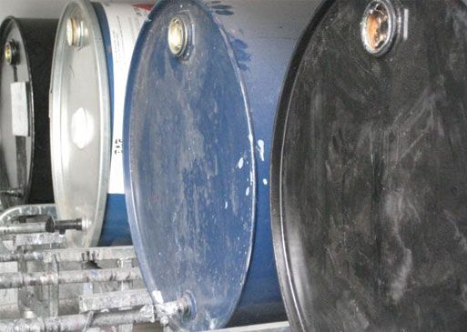 Four industrial drums, varying colors, lined up on a metal shelf.