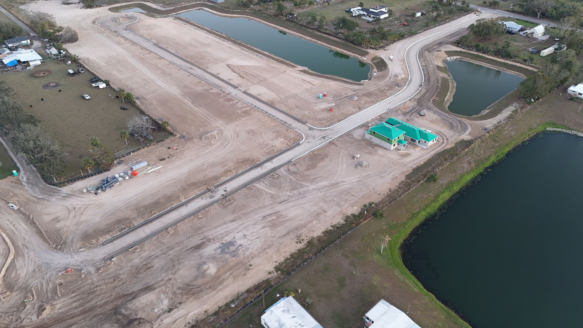 Aerial view of a construction site with dirt roads, ponds, and a partially built building with a green roof.