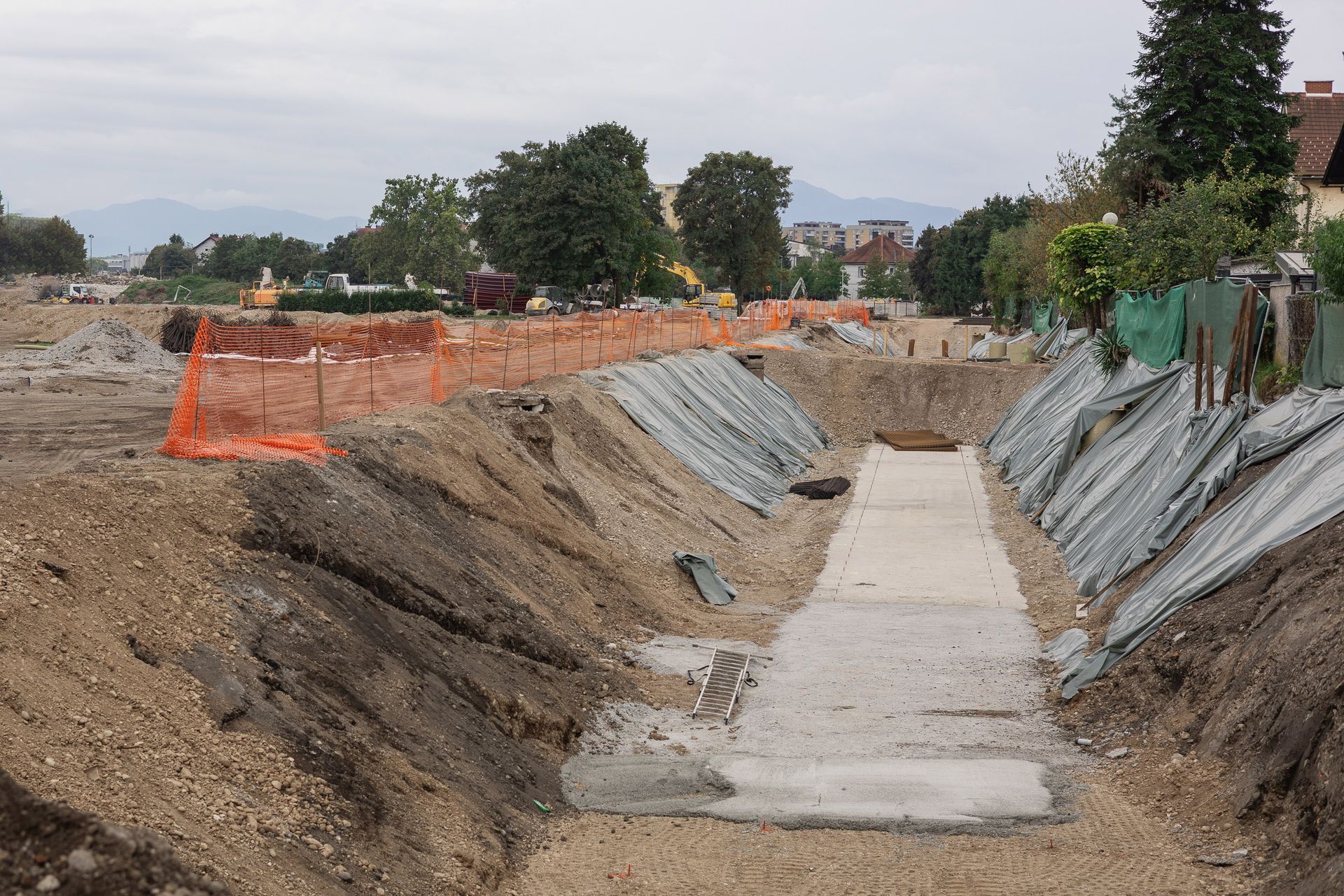 Construction site with a concrete path, dirt embankments, and orange safety fencing.