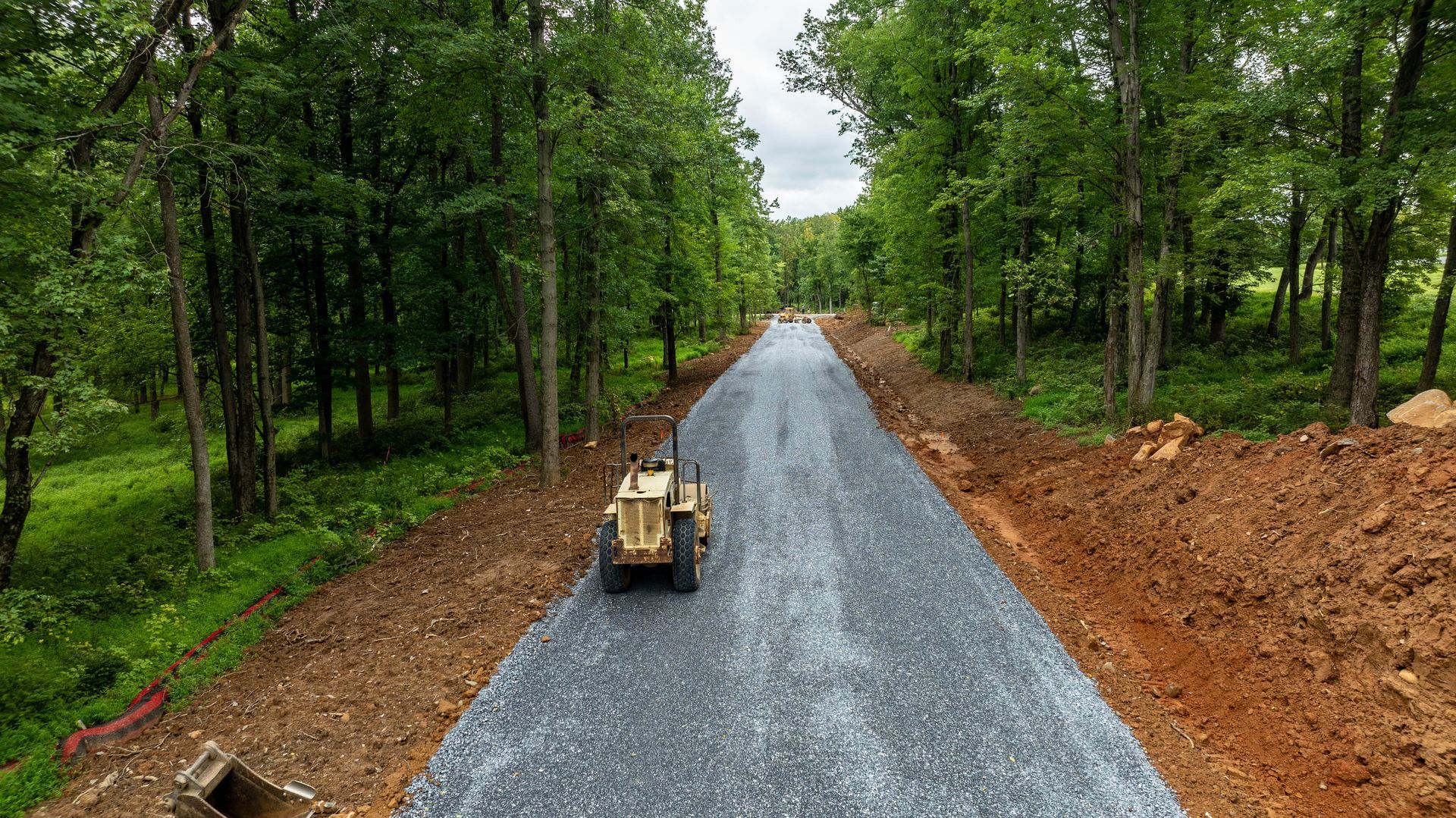 Construction of a gravel road through a wooded area; a yellow bulldozer at work.